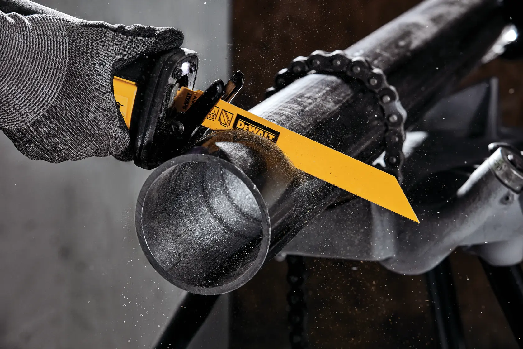 A DEWALT reciprocating saw blade cutting through a metal pipe, with a gloved hand operating the saw.