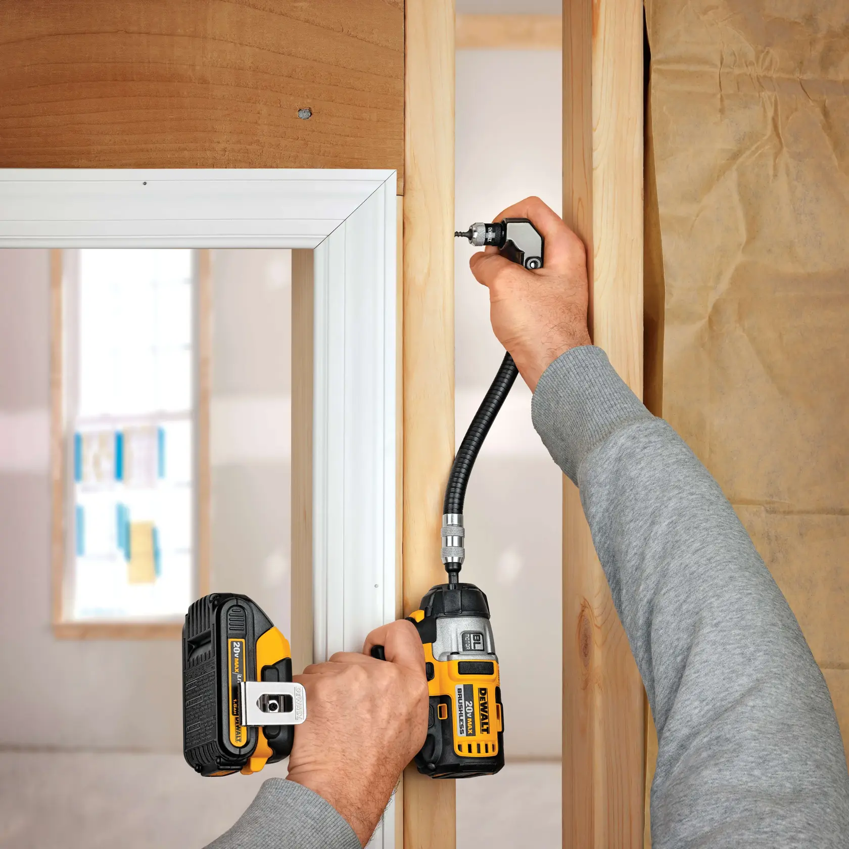 A person uses a DEWALT cordless power drill equipped with a flexible shaft attachment to drive a screw into a wooden door frame during construction or installation work.