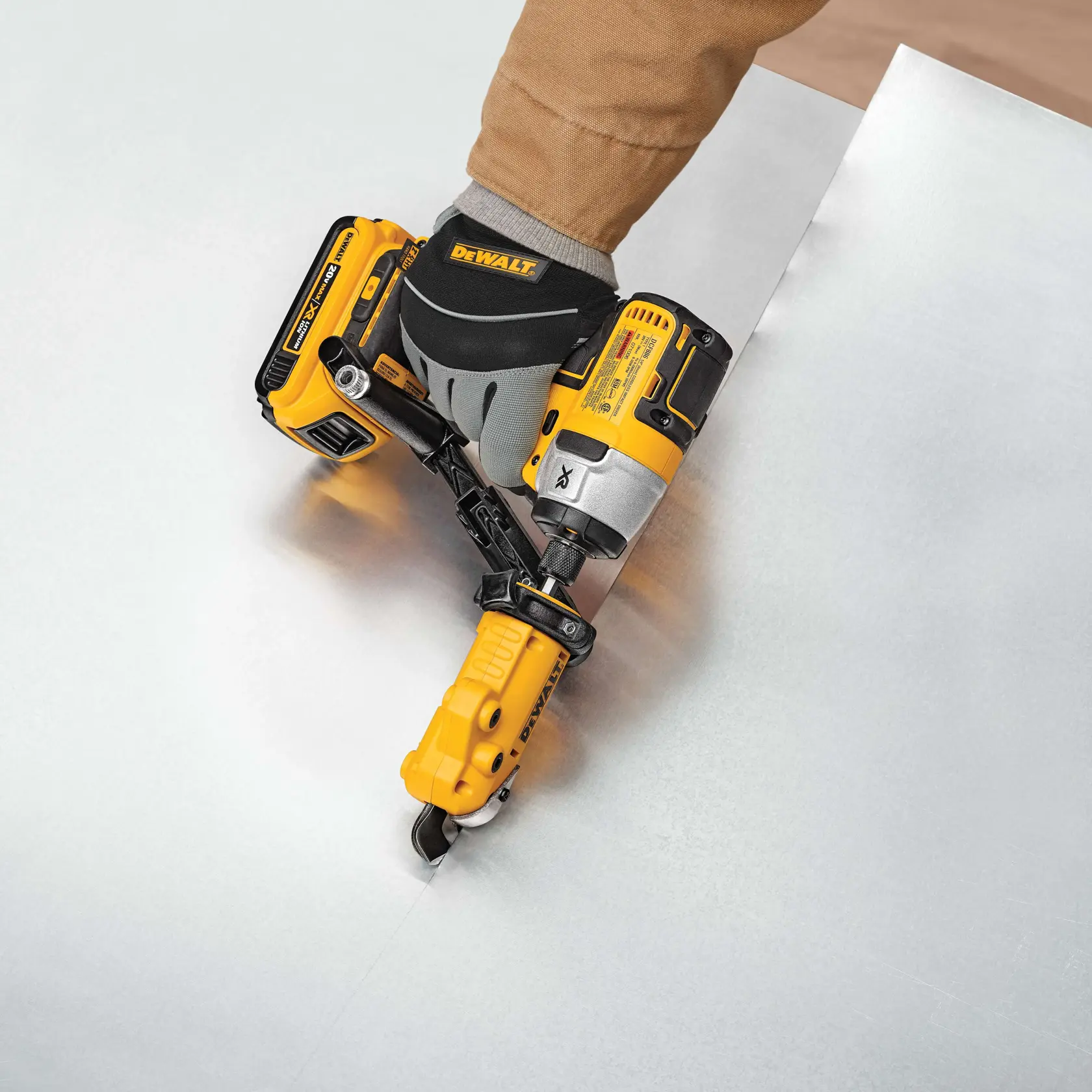 A person wearing a glove operates a yellow DEWALT cordless power tool from the SKU DWASHRIR, designed for cutting sheet metal. The tool is being used to make a precise cut through a silver metal sheet.