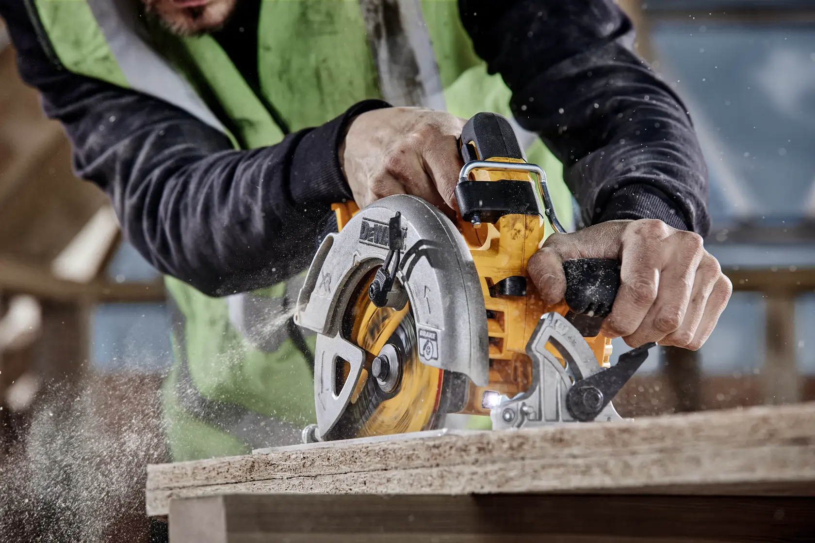 Close-up of a person using a DEWALT circular saw to cut a piece of wood, with sawdust flying as the blade moves through the material.