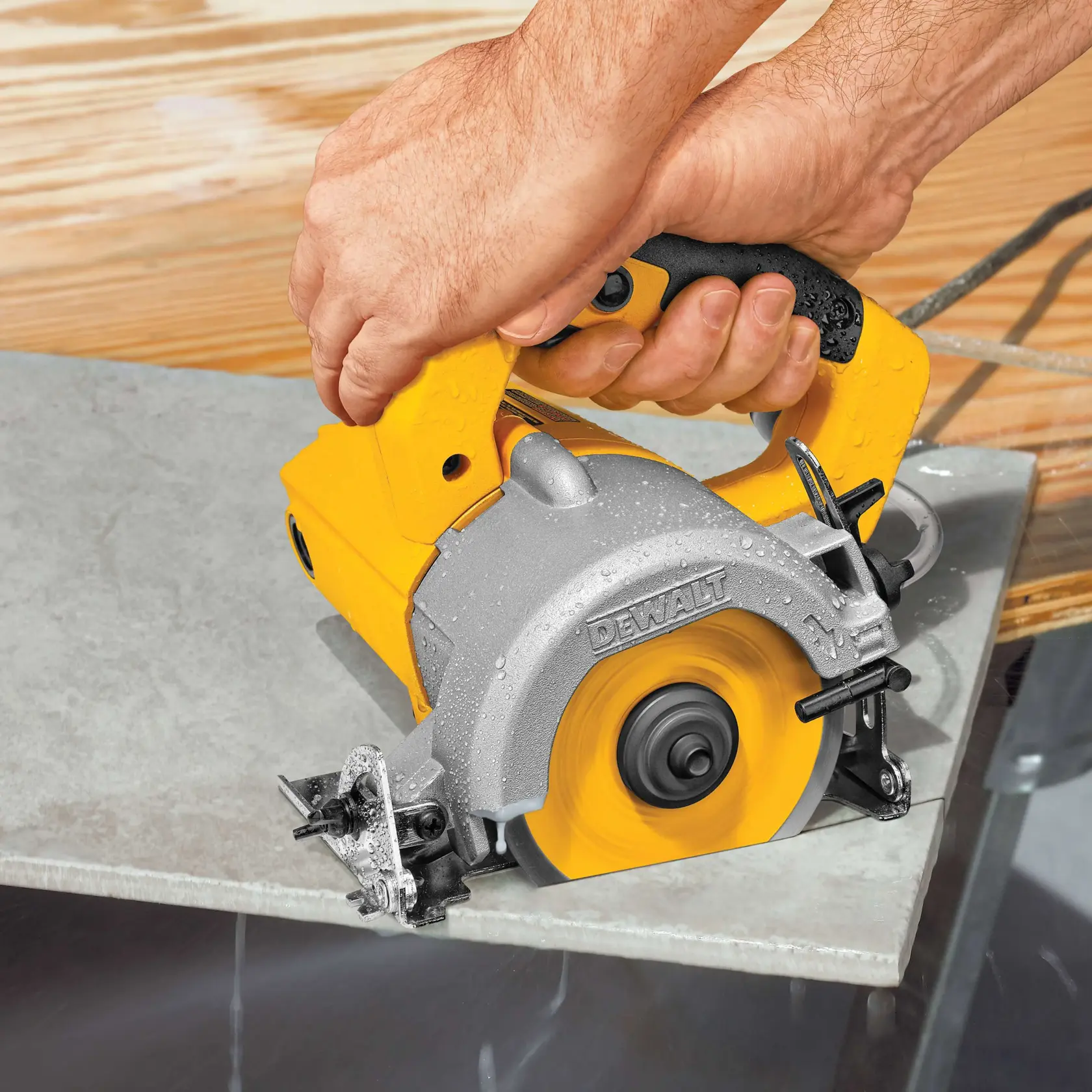 A close-up of a person using a DEWALT handheld tile saw to cut a piece of tile. The saw is yellow and silver, and water is being used to cool the blade during the cutting process.