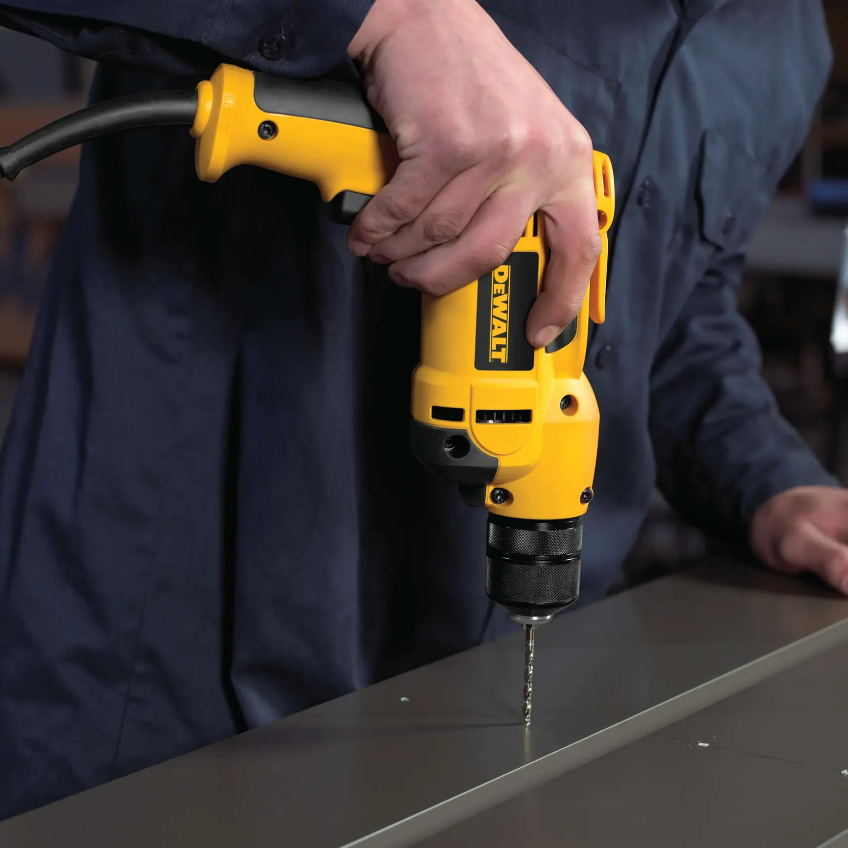 A person using a yellow DEWALT electric drill to drill into a flat surface.