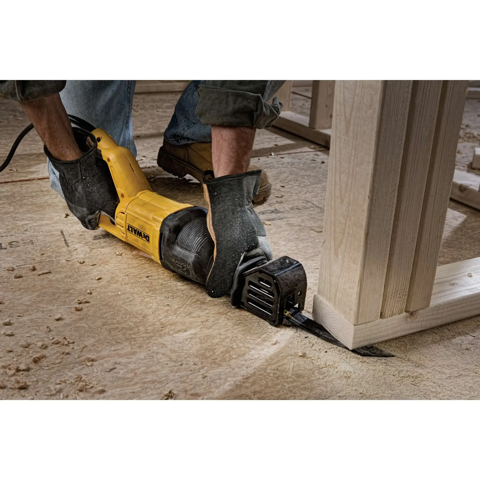 A person wearing work gloves uses a yellow DEWALT reciprocating saw to cut through a wooden board on a construction site.
