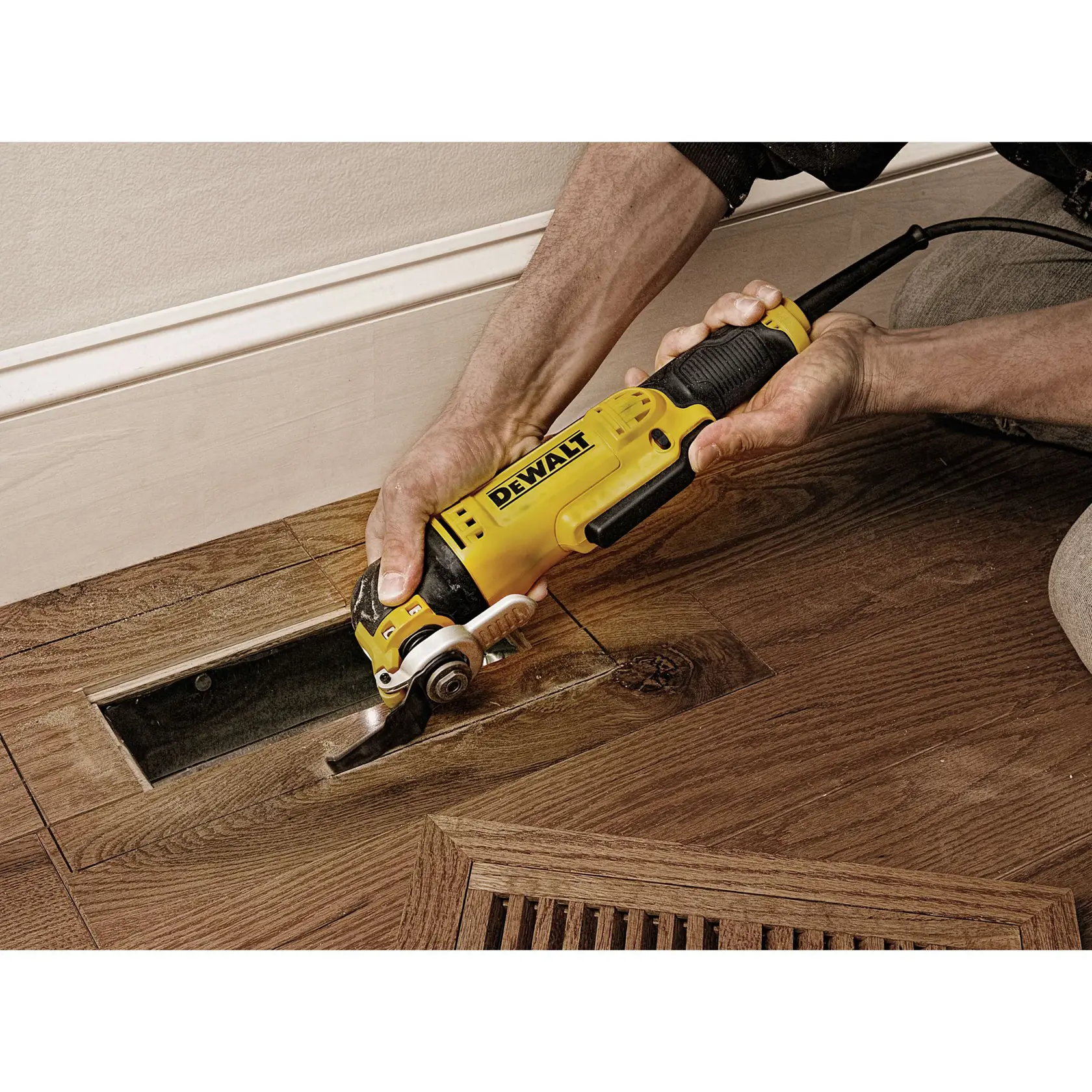 A person using a DEWALT DWE315 oscillating multi-tool to cut a wooden floor panel near a wall.