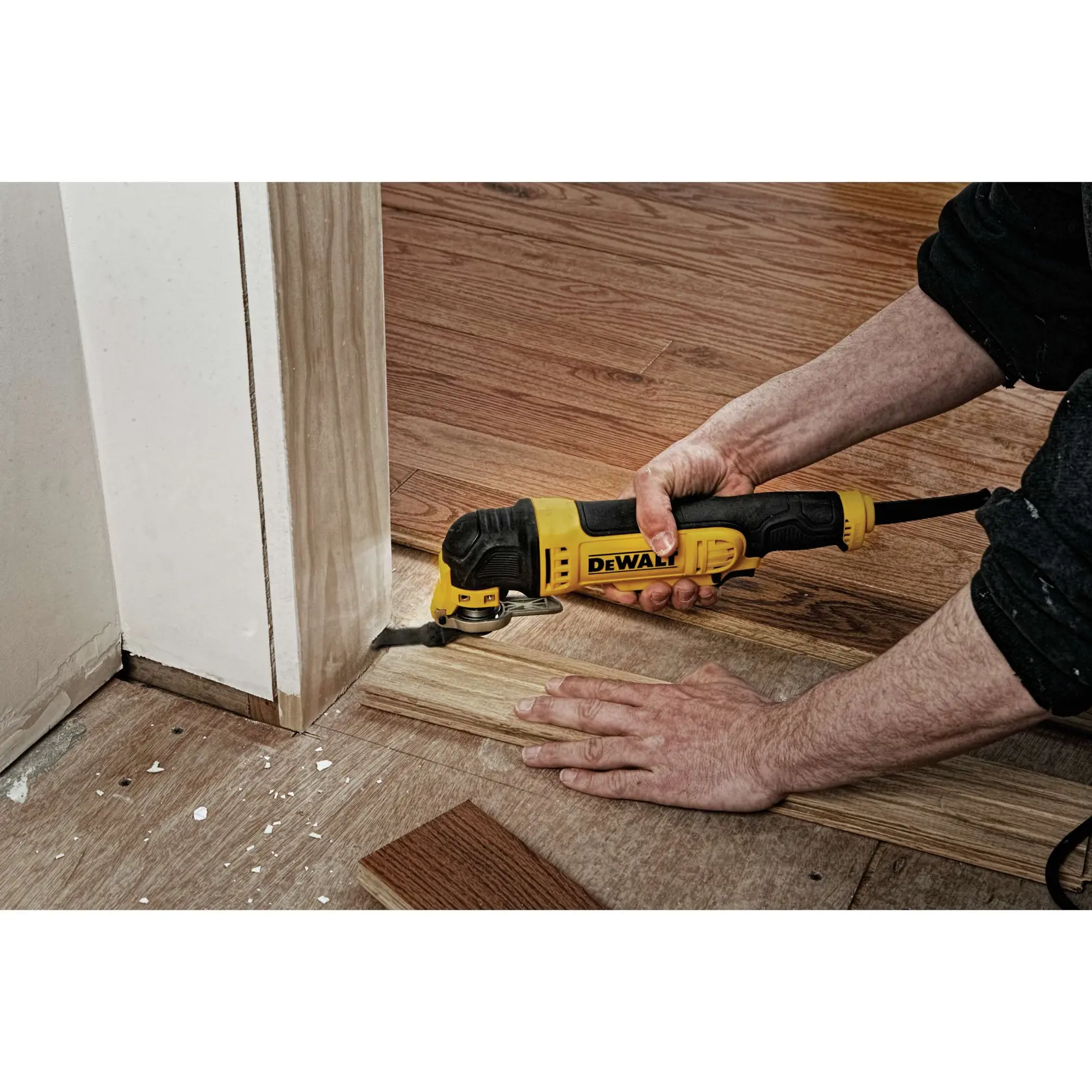 A person uses a yellow and black DEWALT oscillating multi-tool to cut wooden flooring near a doorway.