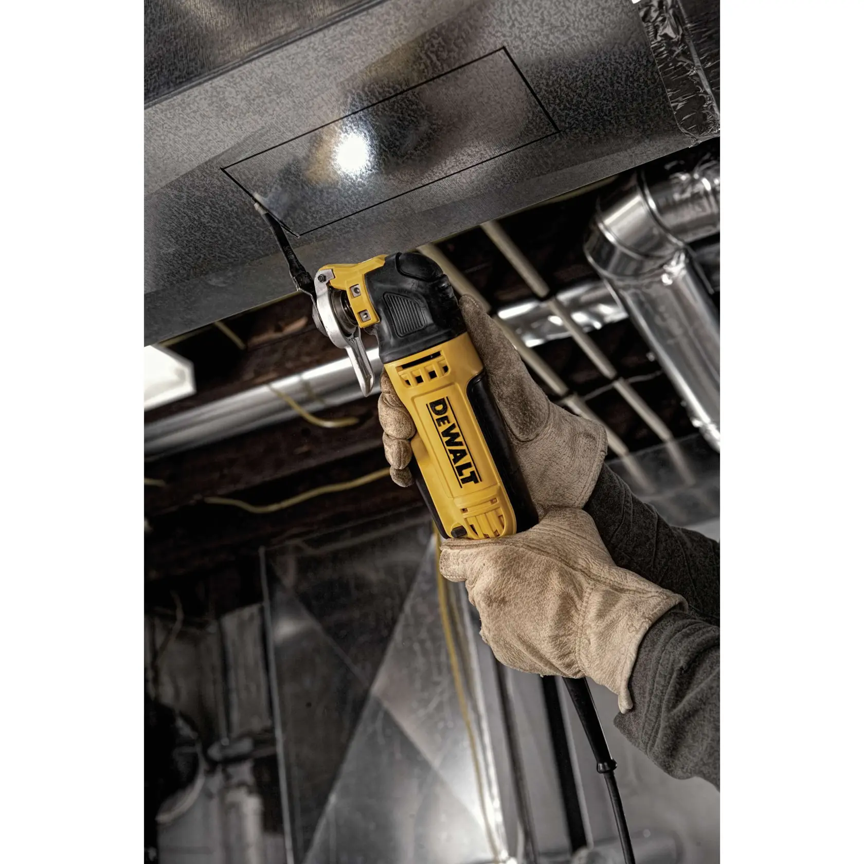 A person wearing work gloves uses a DEWALT DWE315 oscillating multi-tool to cut a square outline in a metal duct. The tool is powered and features a built-in light for precision. The image is set in an industrial environment with visible pipes and ductwork.