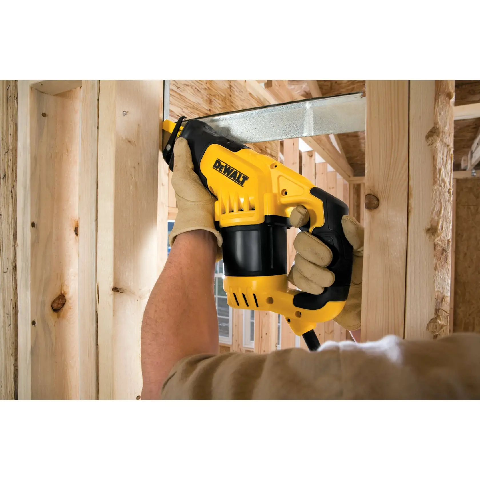 A person wearing work gloves is using a yellow and black DEWALT reciprocating saw to cut a metal beam during construction inside a wooden framed structure.