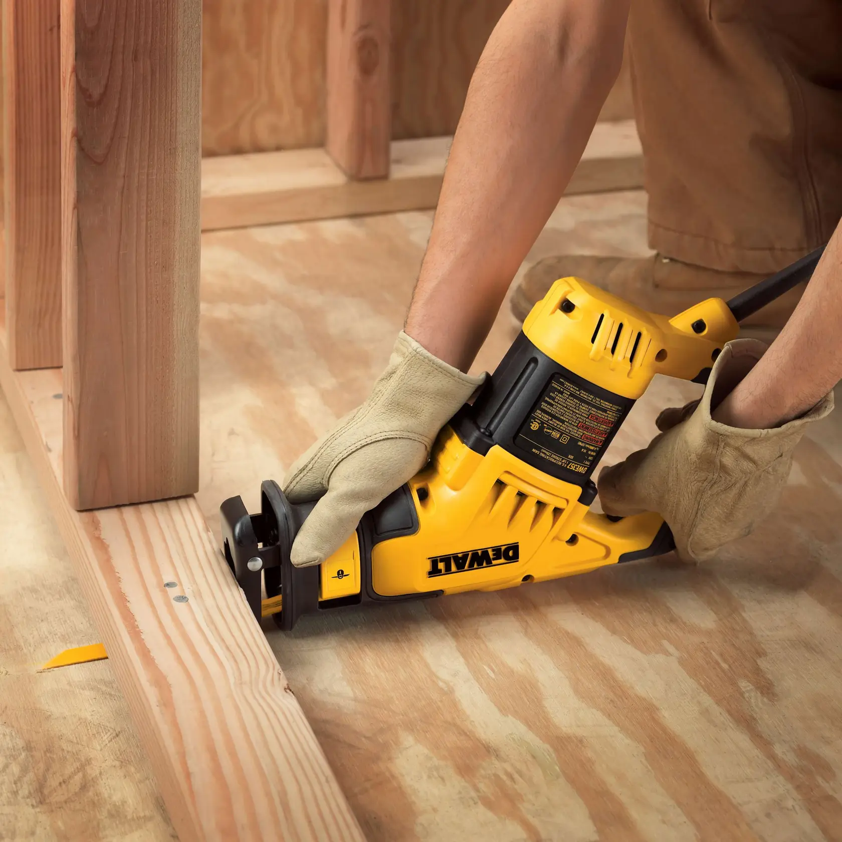 Gloved hands using a DEWALT reciprocating saw to cut wood on a construction site.