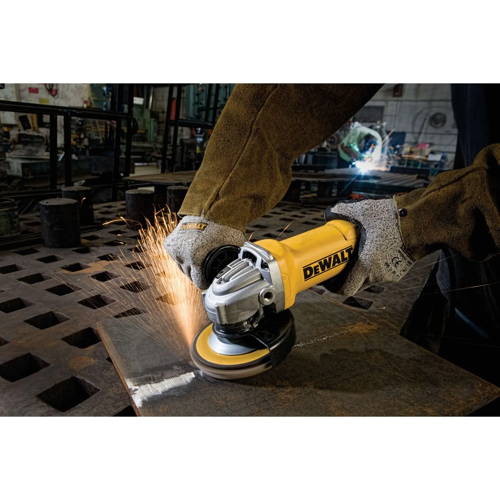 A person wearing protective gloves and clothing uses a yellow DEWALT angle grinder to cut or grind a metal sheet, creating sparks in an industrial workshop setting.