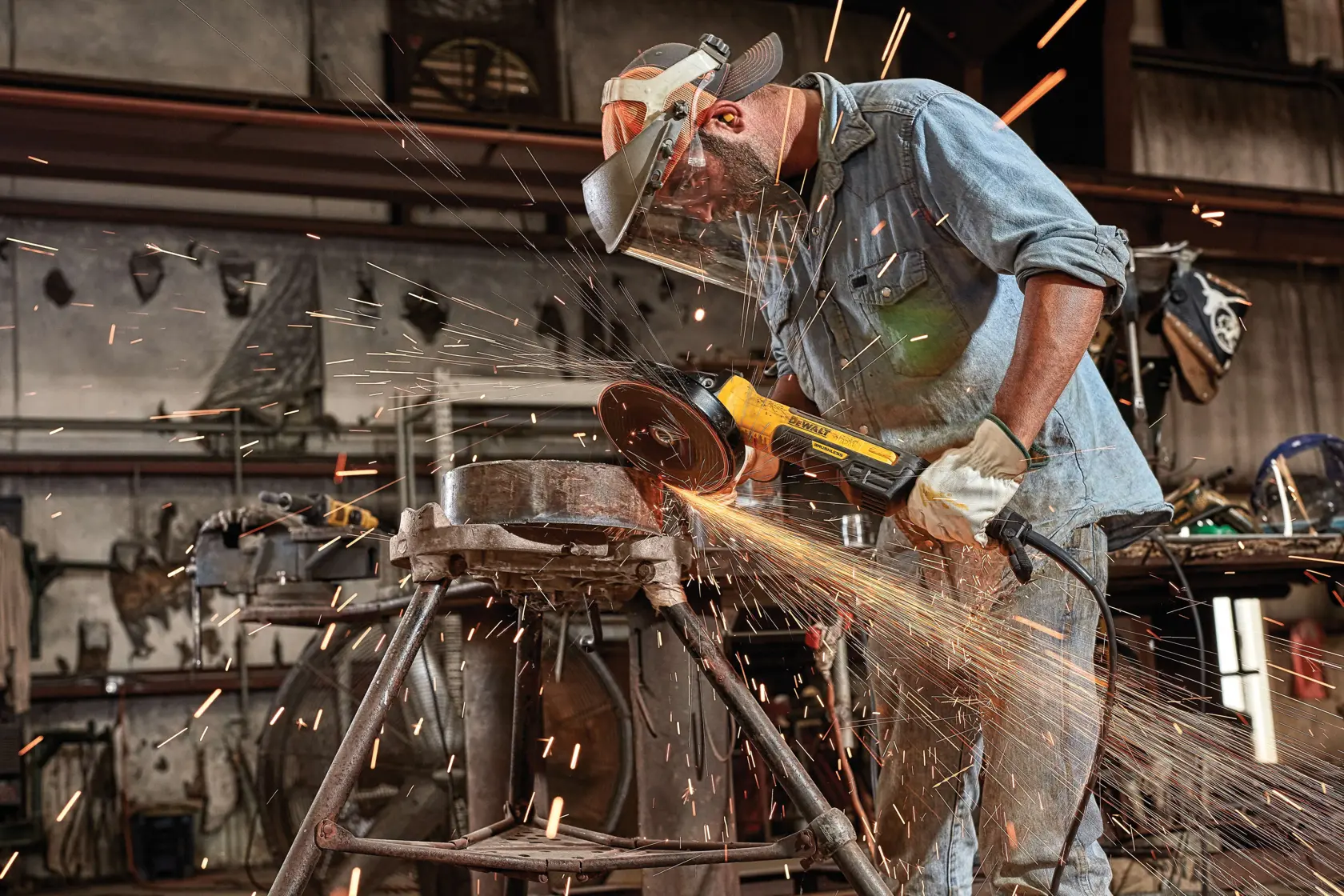 A person wearing safety gear operates a DEWALT angle grinder, cutting metal and producing sparks in an industrial workshop.
