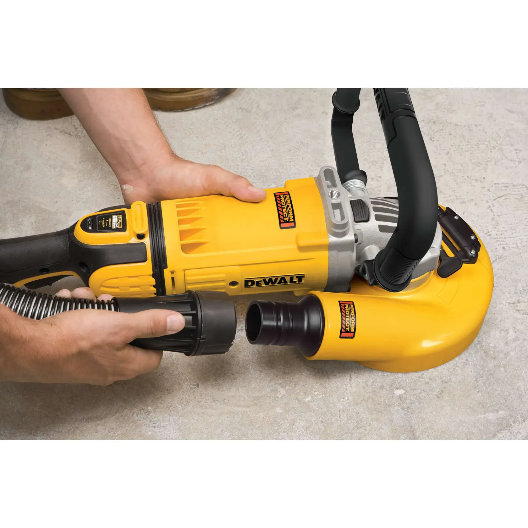 A person wearing protective gear operates a DEWALT industrial vacuum and grinder inside a building under construction. The yellow DEWALT vacuum and grinder are connected, with the vacuum positioned on wheels in the foreground.