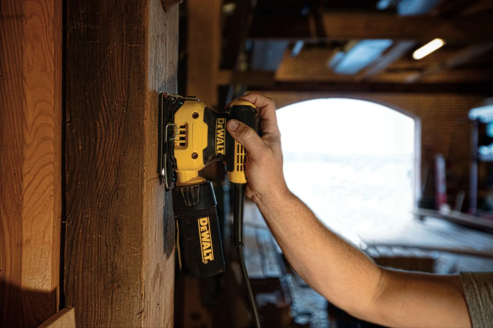 Person using DEWALT DWE6411K sander on wood surface in a workshop setting.