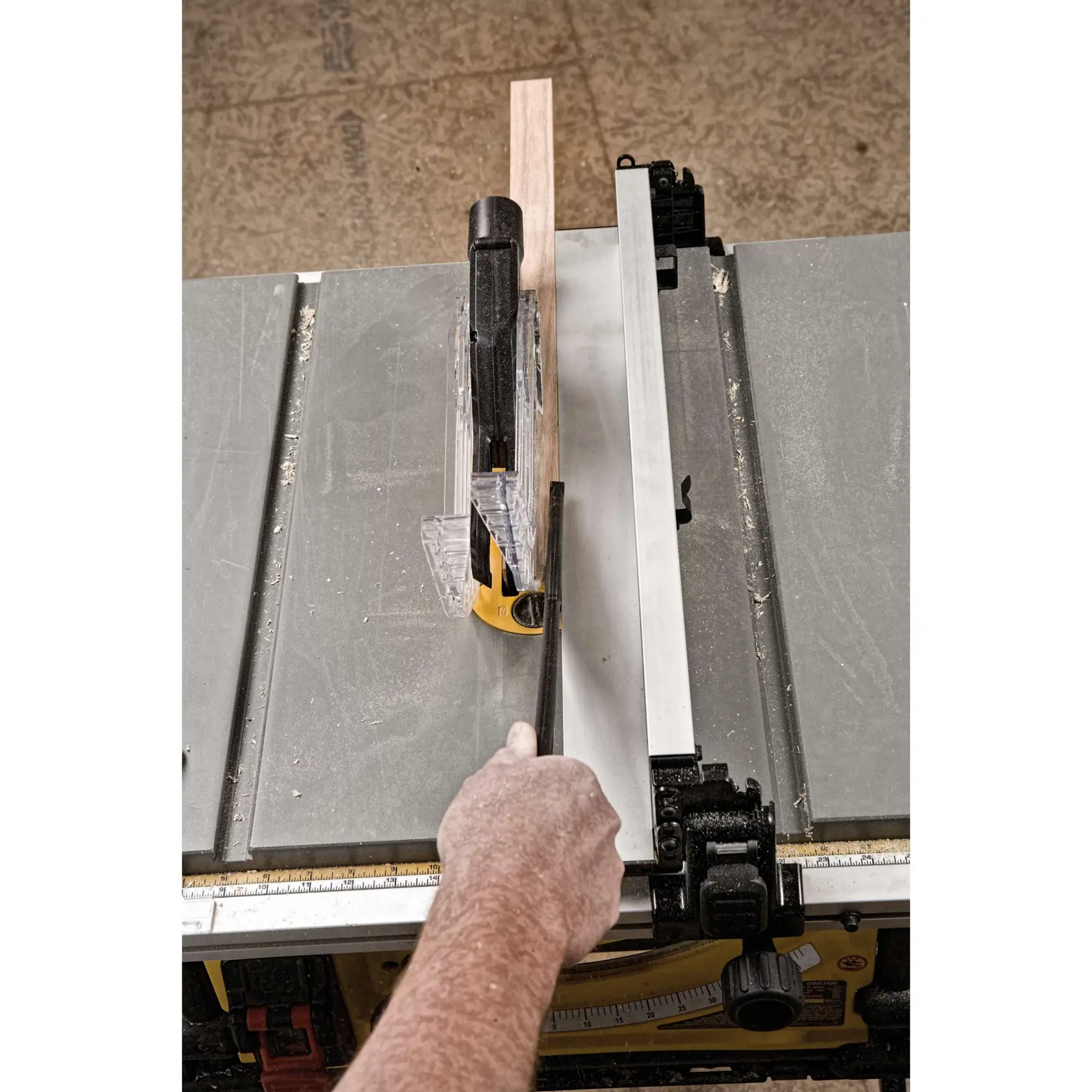 A person using a DEWALT table saw with a push stick to cut a piece of wood, showing a close-up view of the saw blade, safety guard, and fence.