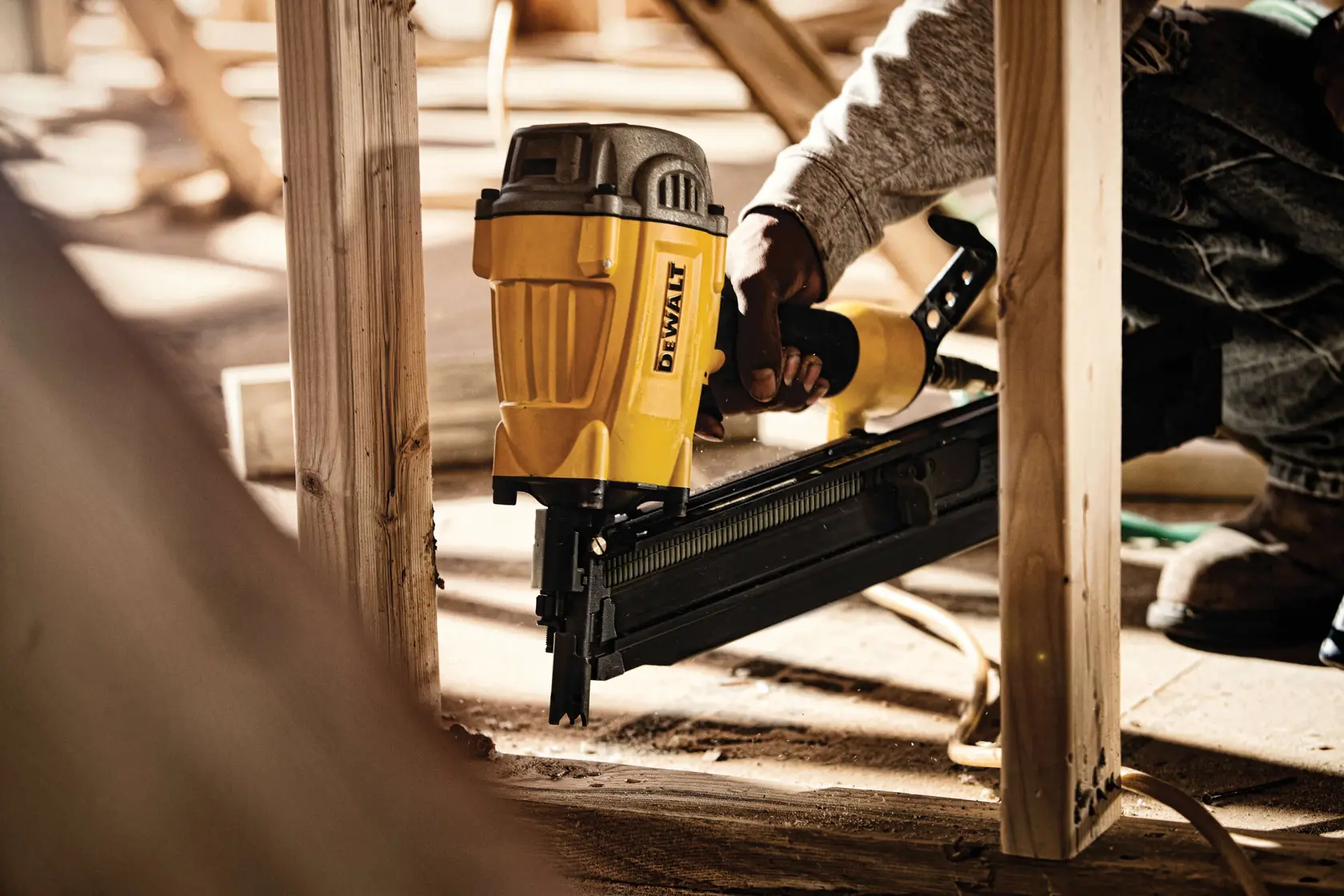 A person using a DEWALT framing nailer to secure wooden beams during construction.