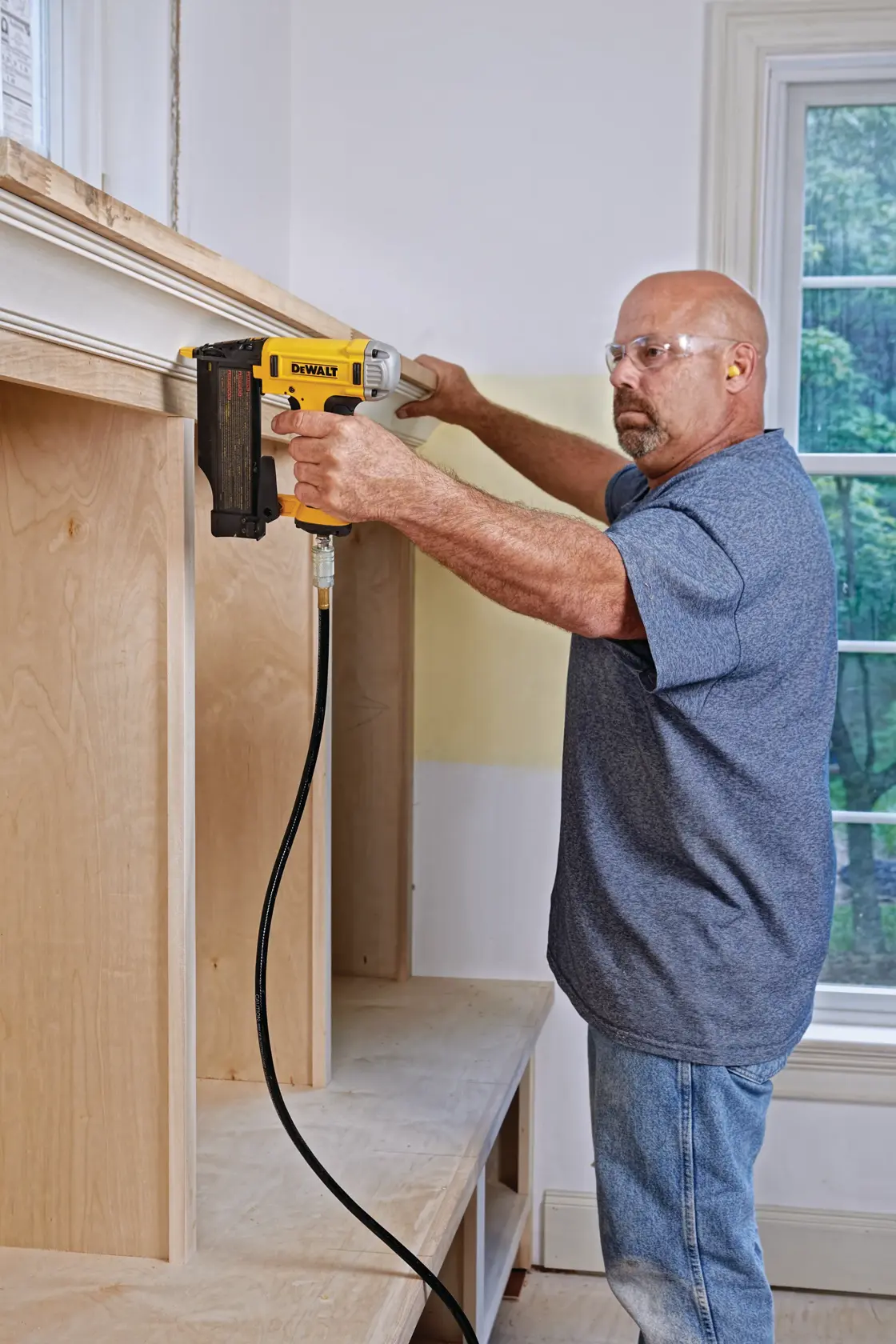 Close-up of a DEWALT nailer driving a 23-gauge, 2-inch nail into trim with a yellow strip at the bottom that reads: 'DRIVES 23GA 2'' NAILS'.