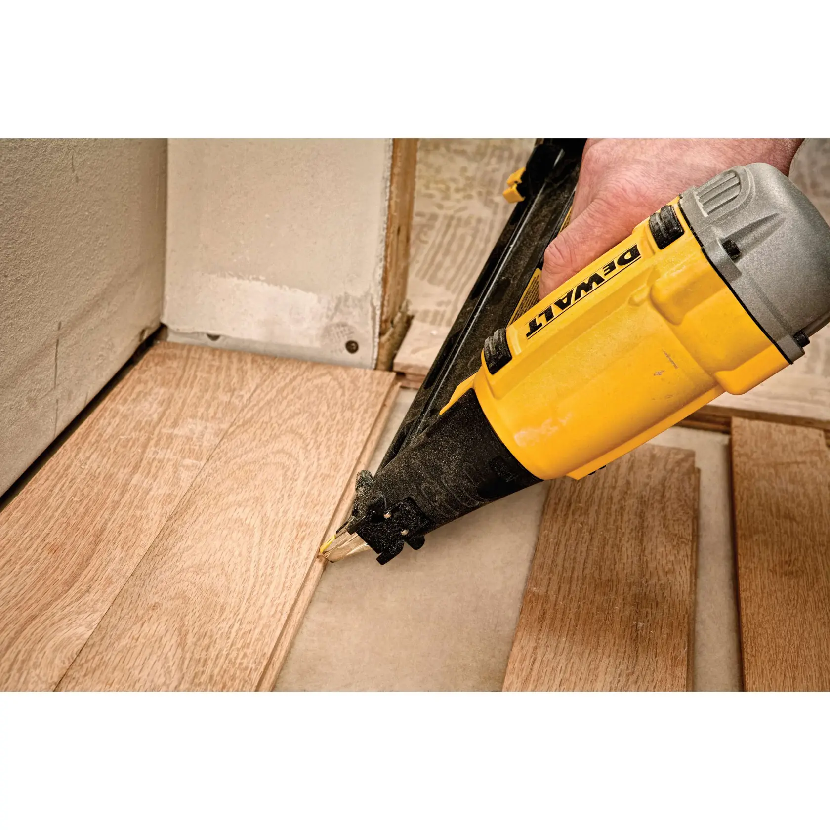 A person using a yellow DEWALT nail gun to install wooden flooring near a wall.
