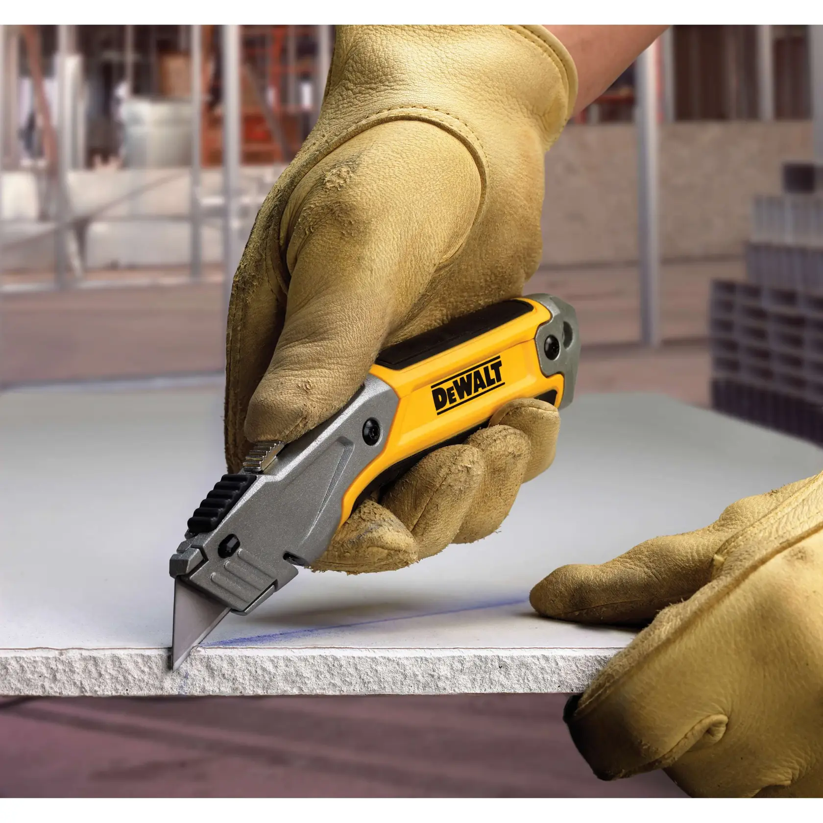A person wearing work gloves uses a DEWALT utility knife to cut a piece of drywall on a construction site.