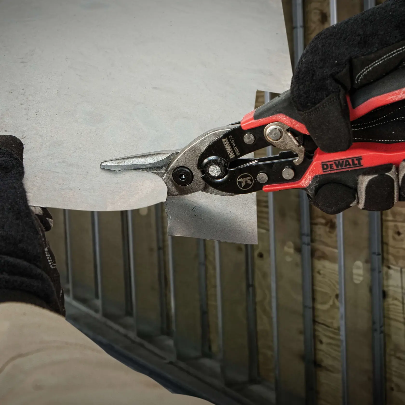 A person wearing gloves is using a DEWALT metal cutting tool to cut through a sheet of metal.