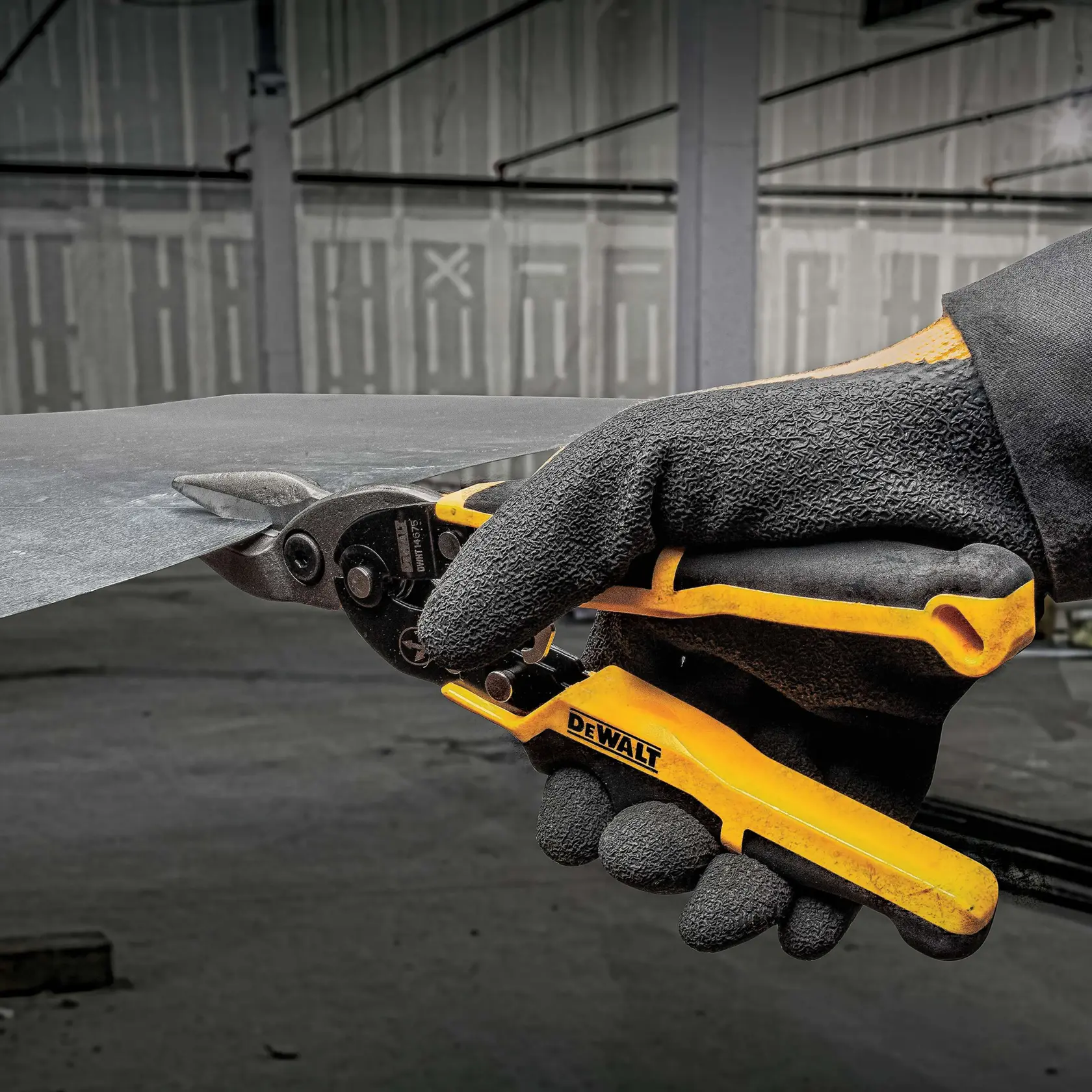 A gloved hand using a DEWALT metal cutting snip to cut a sheet of metal in an industrial environment.