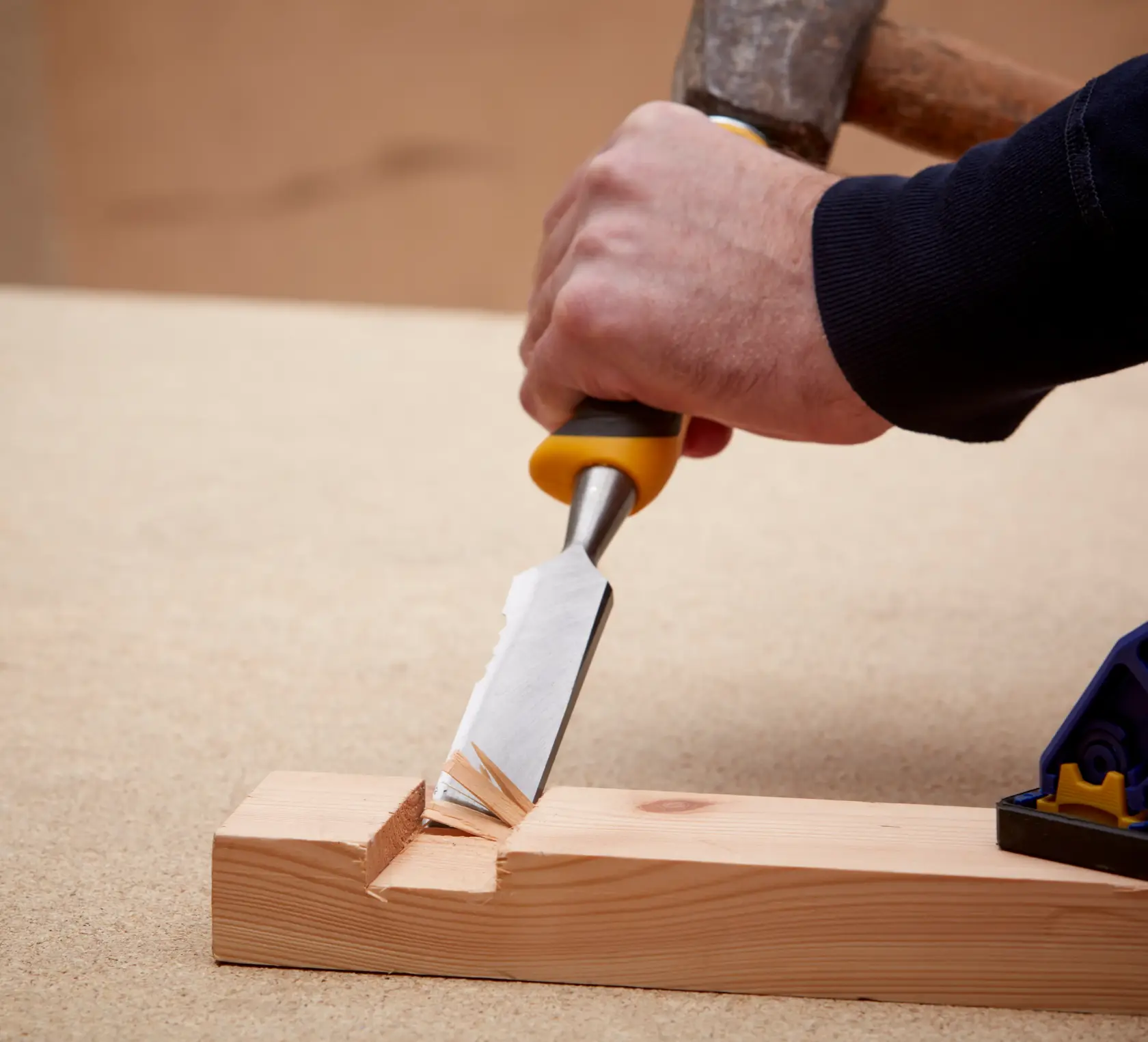 A hand uses a DEWALT chisel with yellow handle to carve wood, creating a notch in a wooden plank.