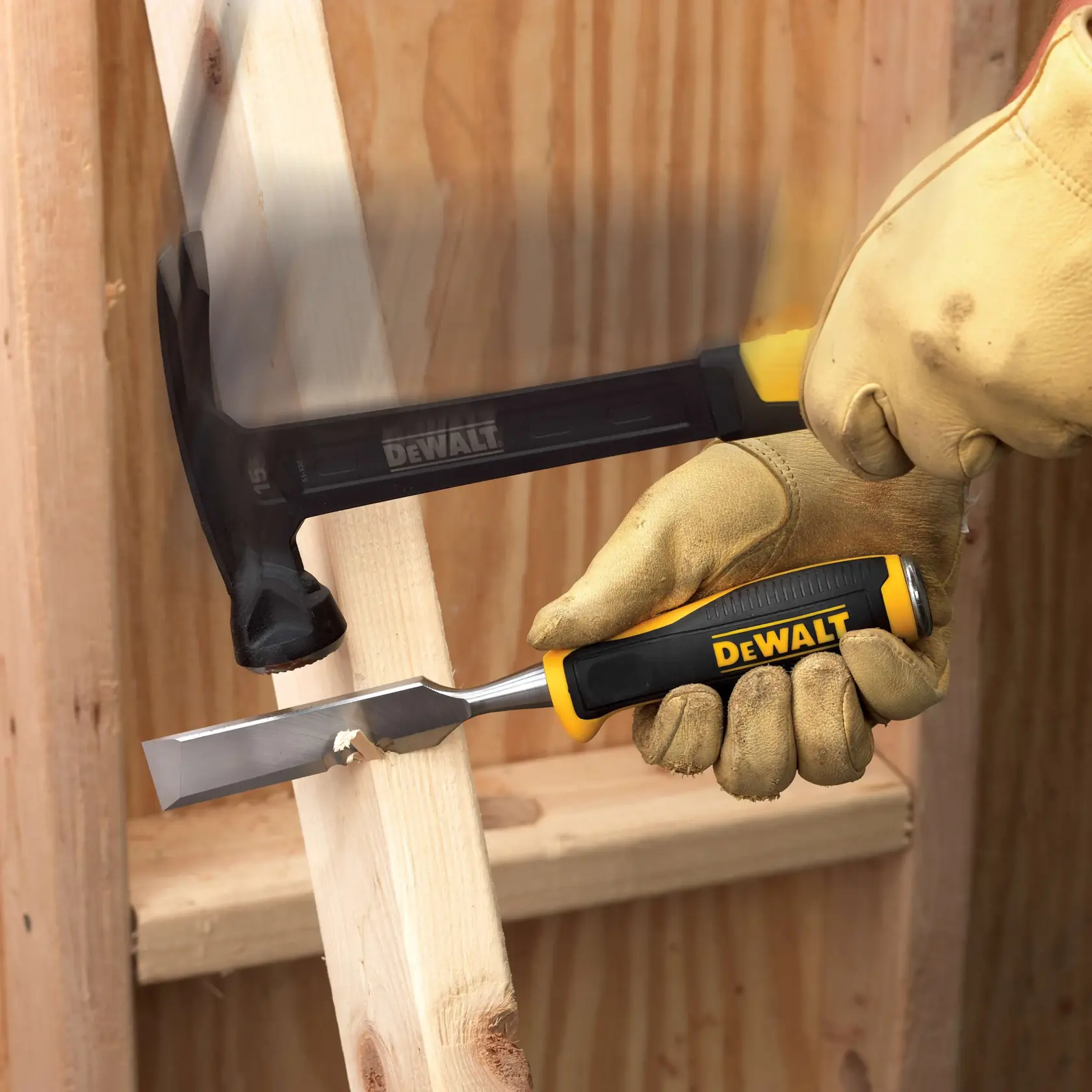A gloved hand holds a DEWALT wood chisel against a piece of wood, while another hand uses a DEWALT hammer to strike the chisel for woodworking purposes. Both tools feature the yellow and black DEWALT branding.