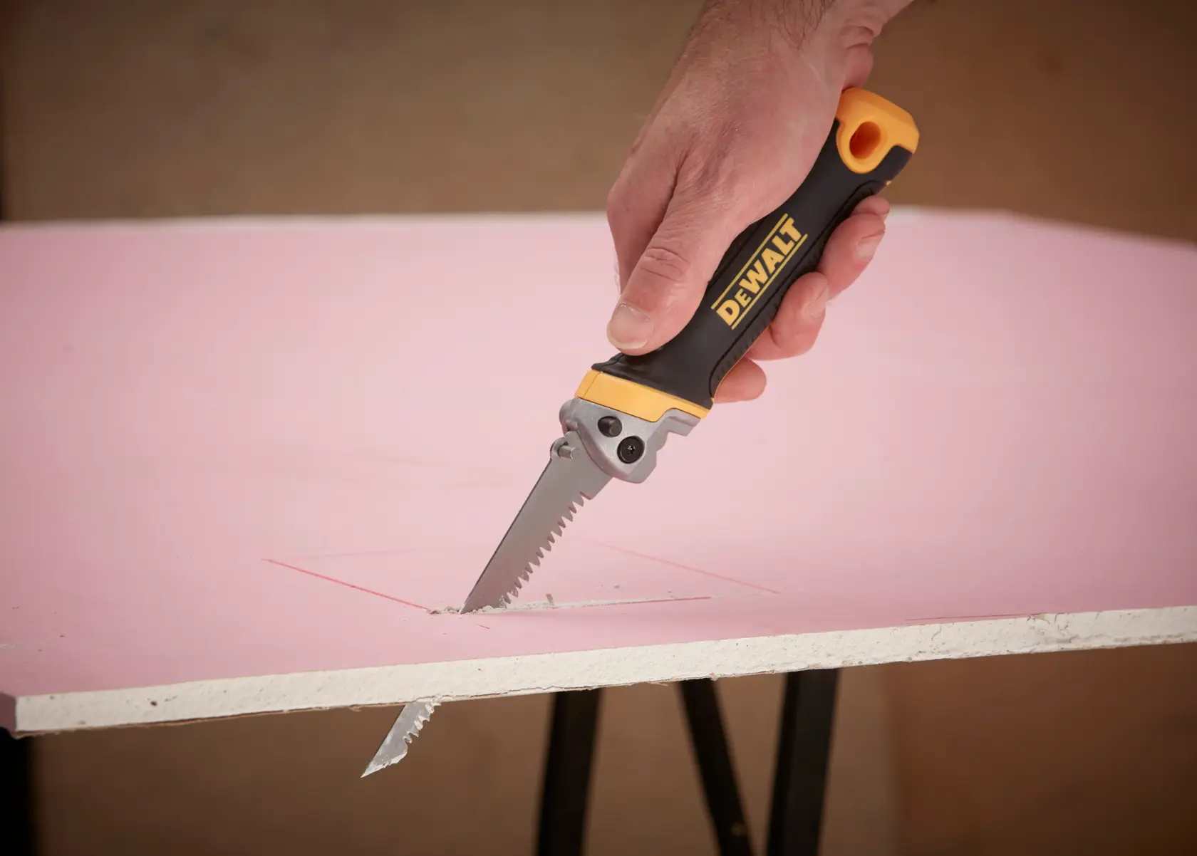 Hand uses DEWALT folding saw to cut rectangular shape in pink drywall sheet.