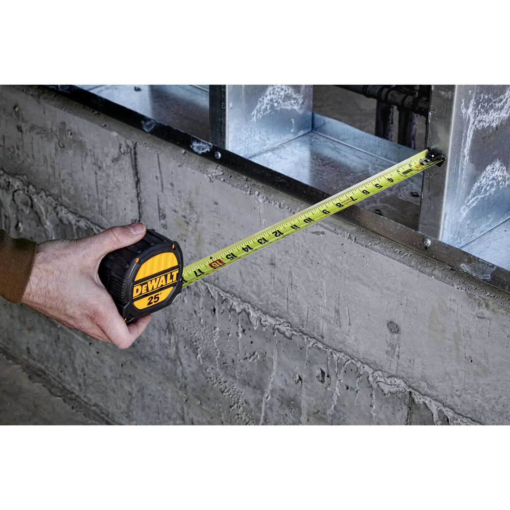 A person using a DEWALT 25-foot tape measure to measure a distance on a concrete construction site.