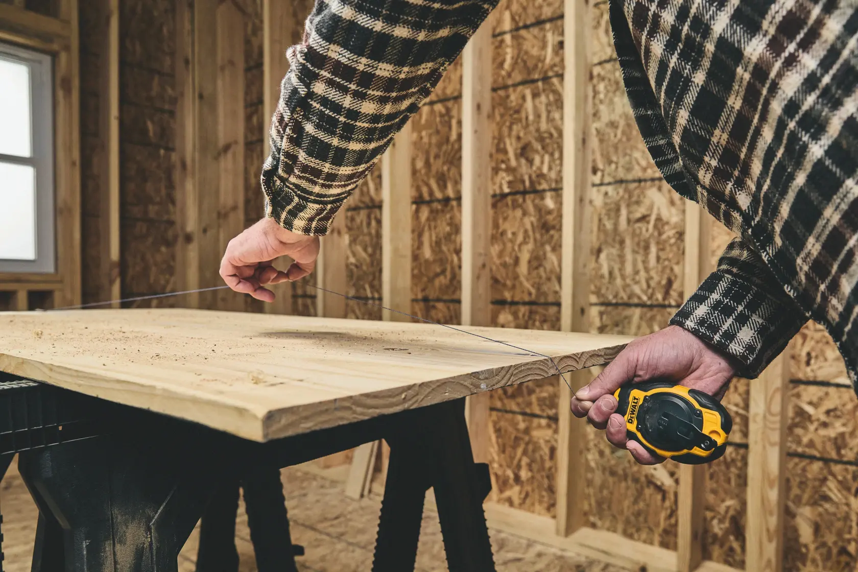 Person using DEWALT chalk line tool to mark a straight line on a wooden board in a workshop.