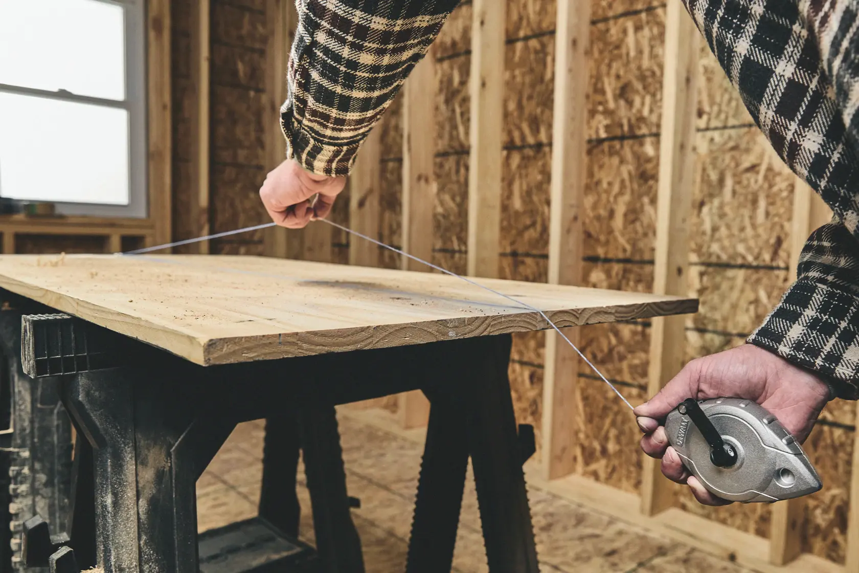 A person uses a DEWALT chalk line tool to mark a straight line across a wooden board in a construction setting.