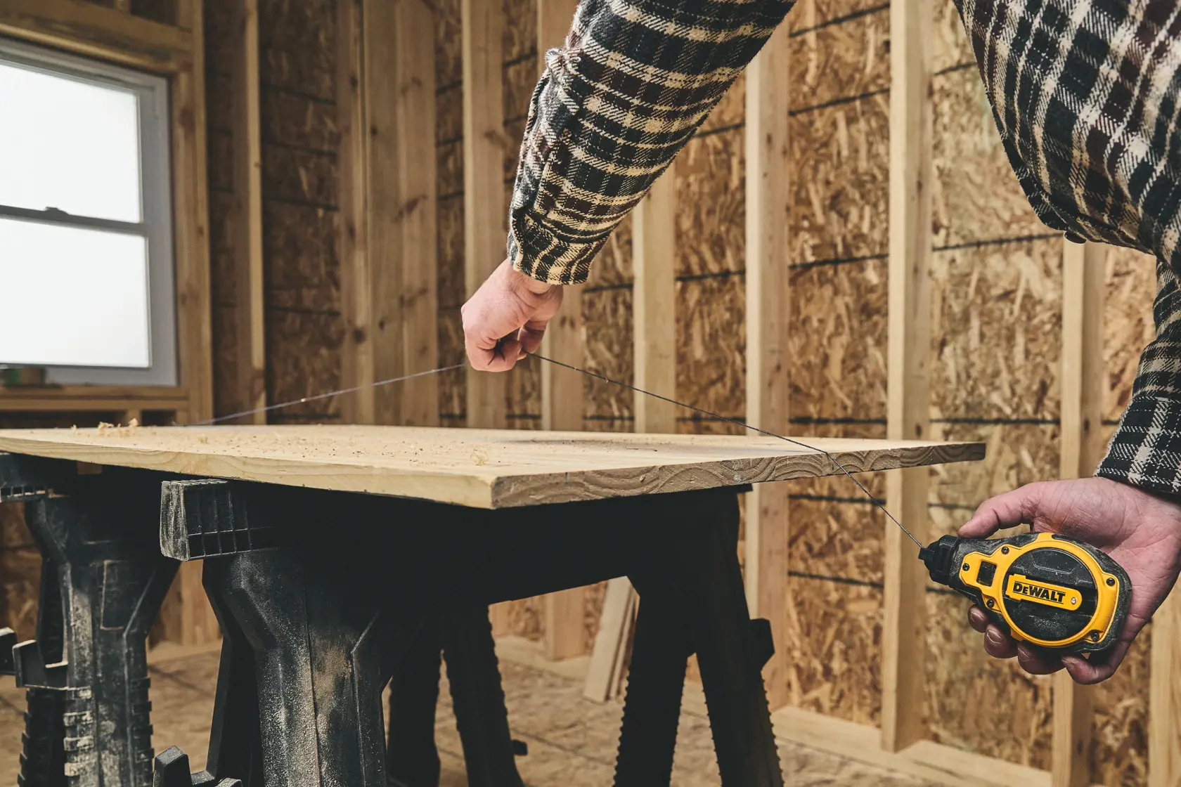 Person marking wood with a DEWALT chalk line tool in a partially finished room.
