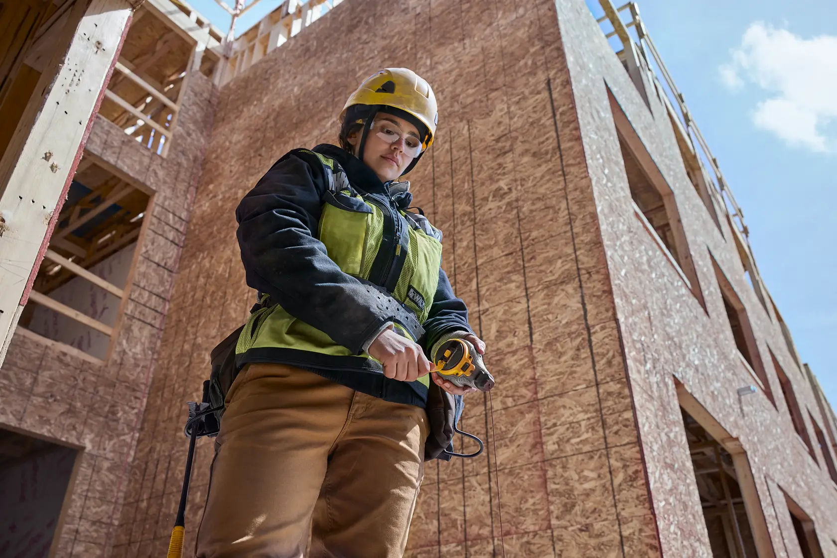 Construction worker holding a DEWALT tape measure at a building site with unfinished walls.