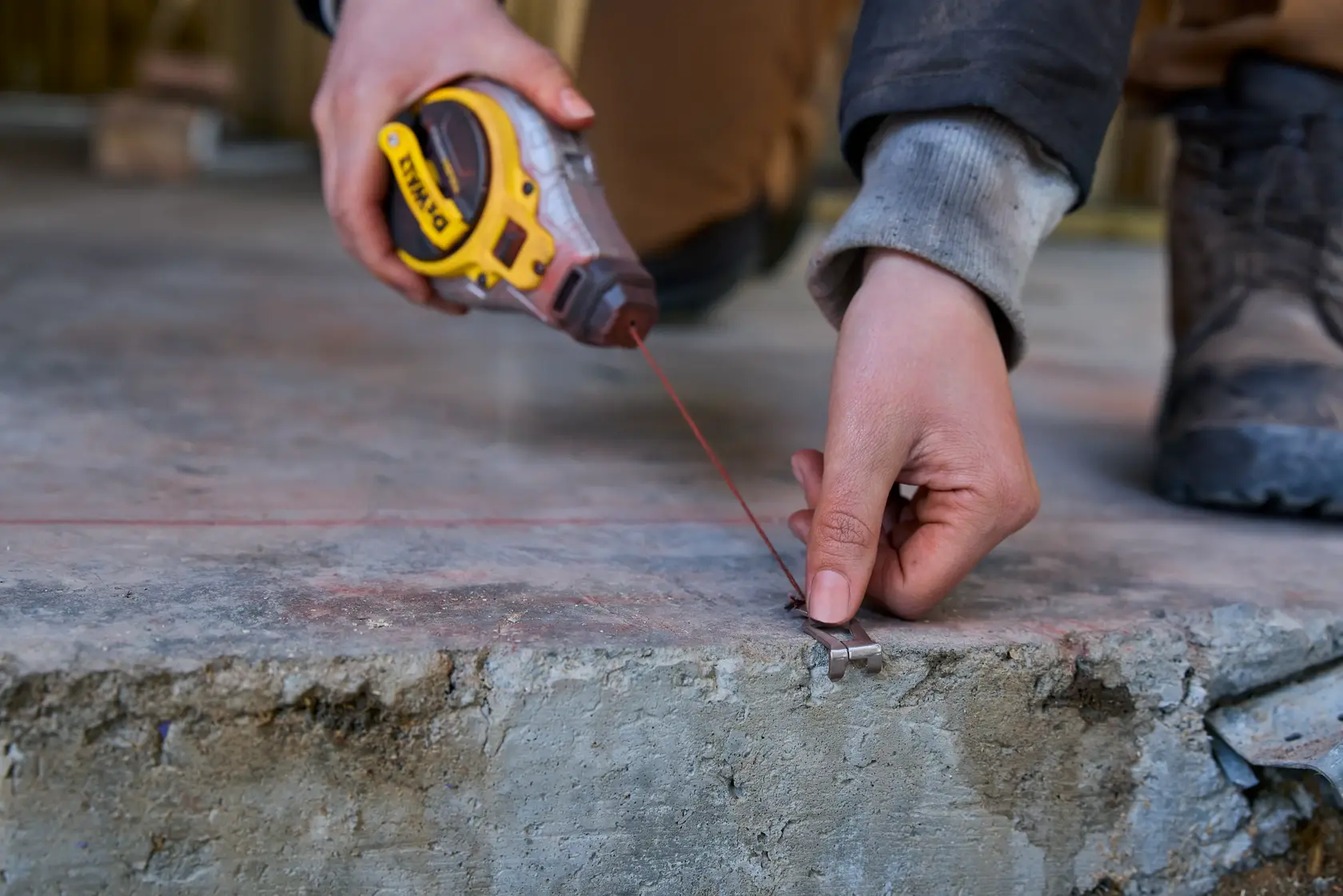 Person uses DEWALT chalk line tool to mark a straight line on a concrete surface during construction.