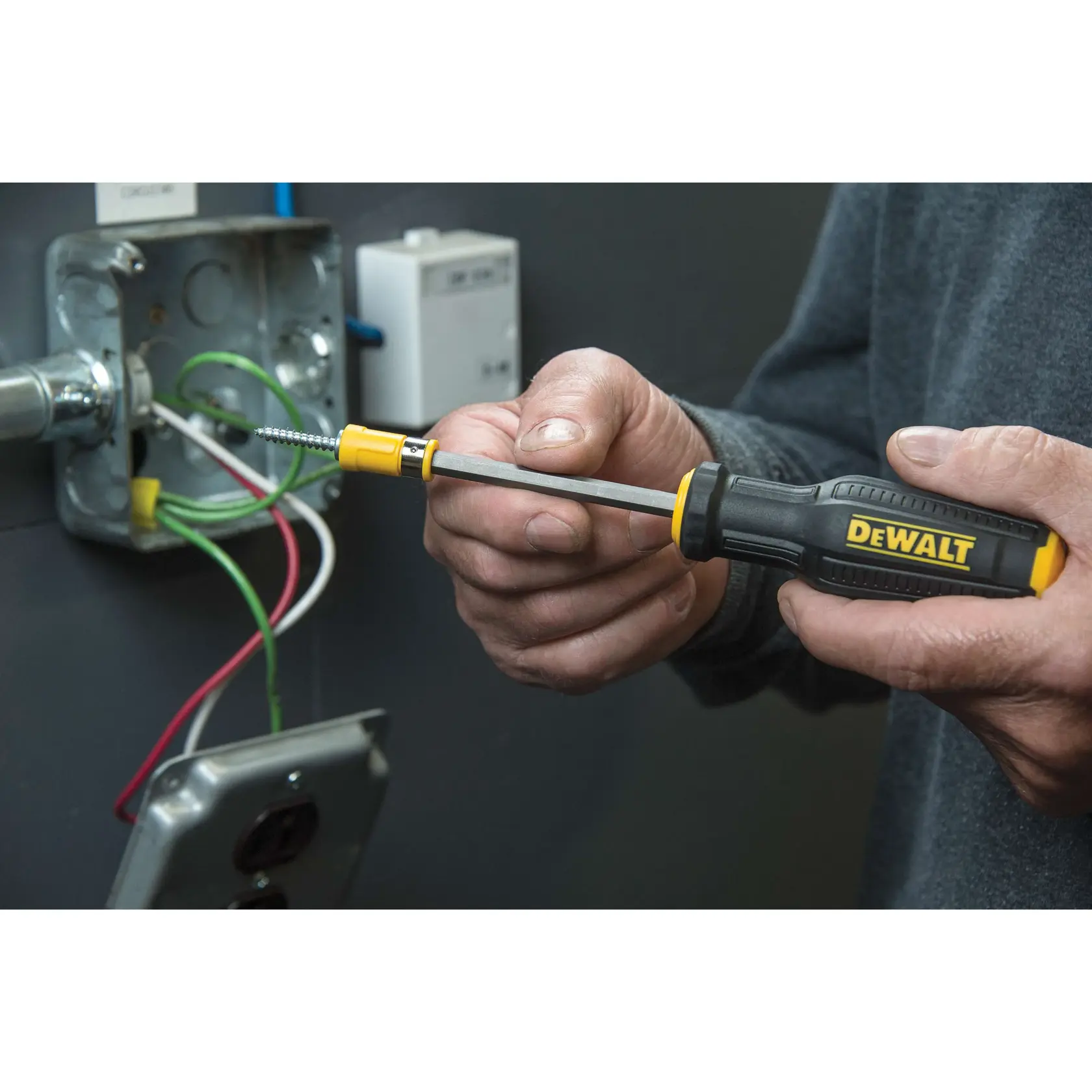 A person is using a DEWALT screwdriver to work on an electrical junction box, with visible green, white, and red wires.