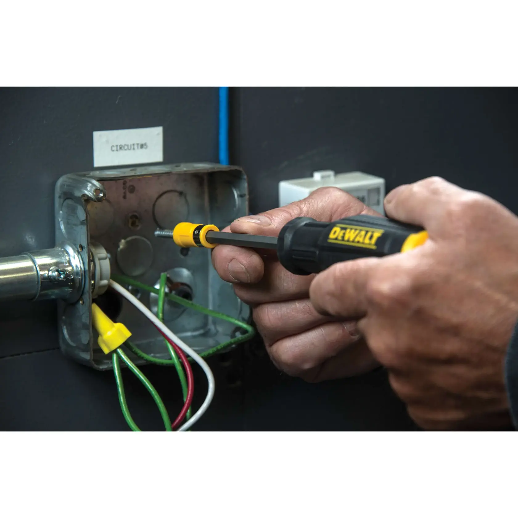 A person using a DEWALT screwdriver to work on electrical wiring inside a metal junction box.