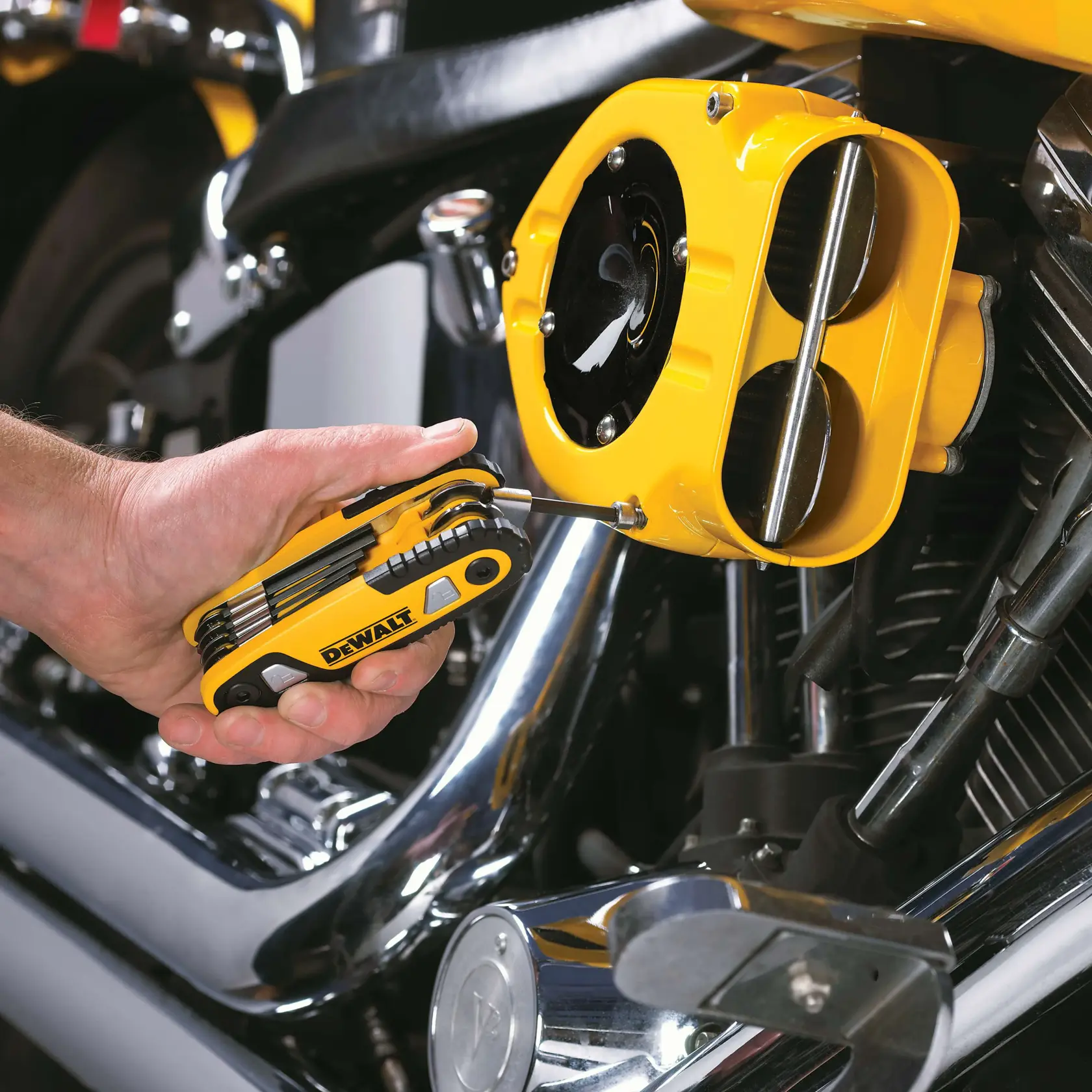 A hand using a DEWALT multi-tool to adjust a screw on a yellow motorcycle engine component.