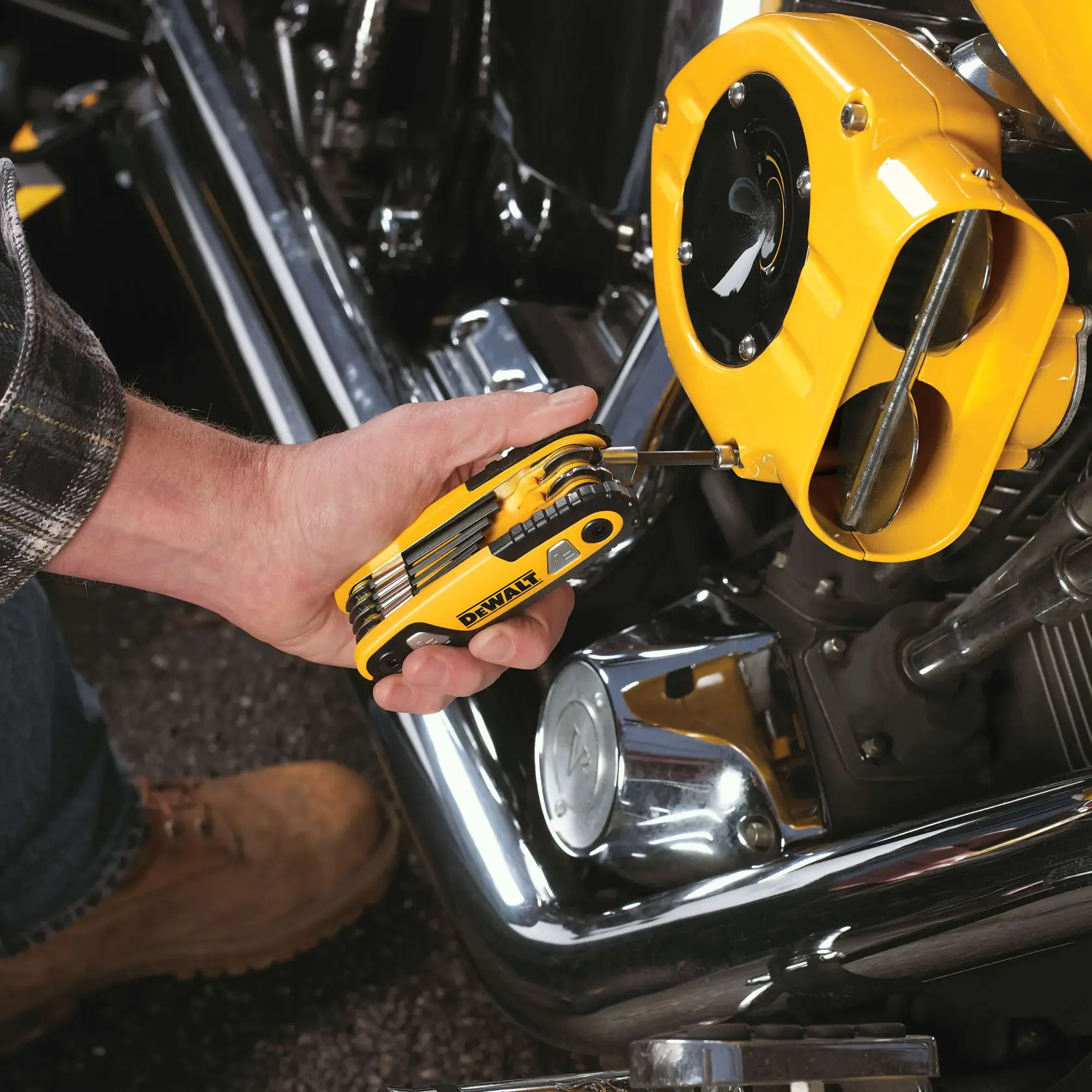 A person is using a yellow DEWALT multi-tool to adjust or fix a part on a motorcycle engine. The tool is being applied to a screw on a yellow engine cover.