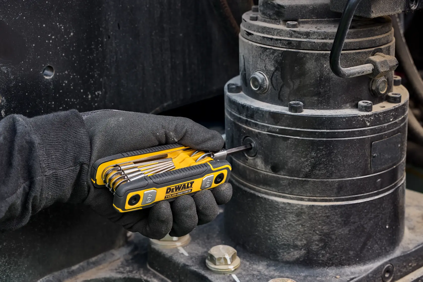 A gloved hand using a DEWALT folding hex key set to tighten a bolt on industrial machinery.