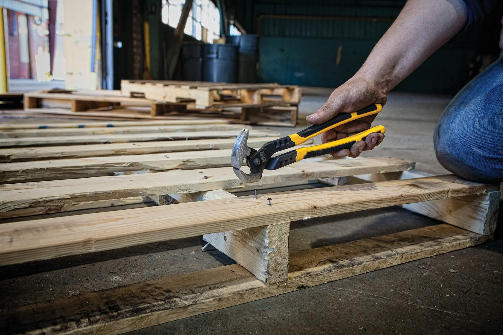 A person uses a DEWALT bolt cutter tool to remove nails from a wooden pallet in an industrial setting.