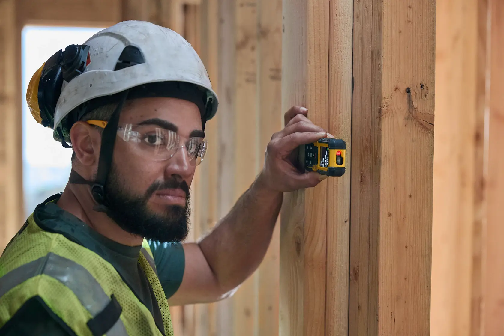 Worker uses DEWALT laser distance measurer on wooden beam at construction site.