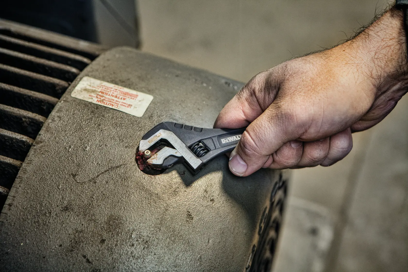 A hand holding a DEWALT adjustable wrench is tightening or loosening a bolt on a large industrial machine.
