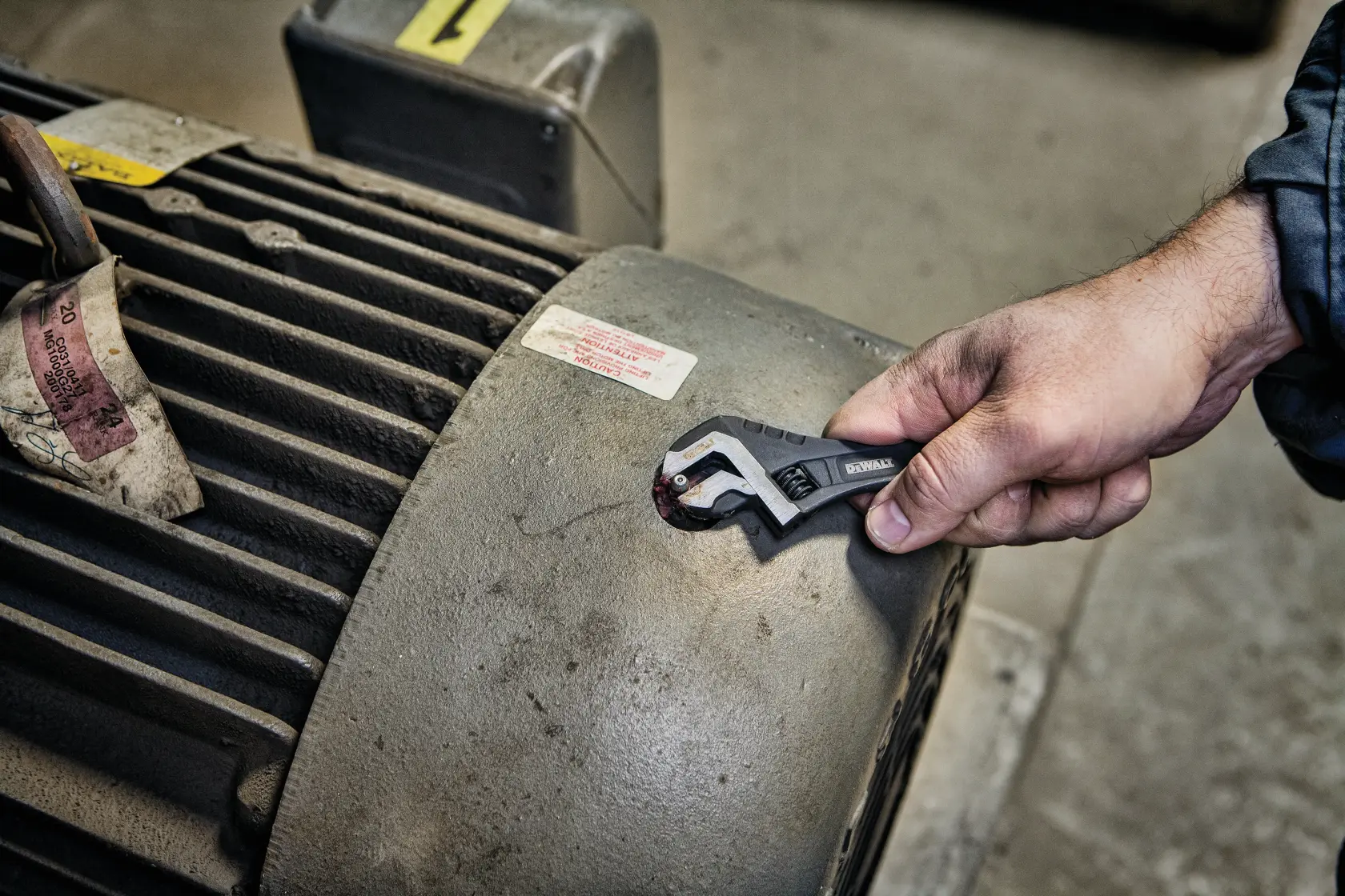A hand using a DEWALT adjustable wrench to tighten a bolt on a large industrial machine.