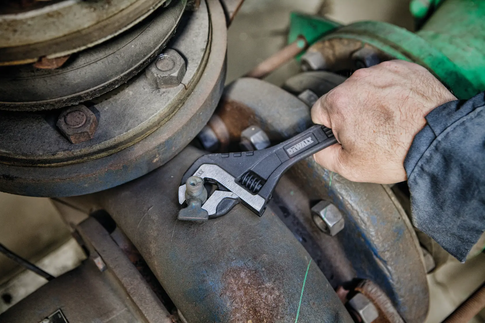 A person uses a DEWALT adjustable wrench to tighten a bolt on industrial machinery.