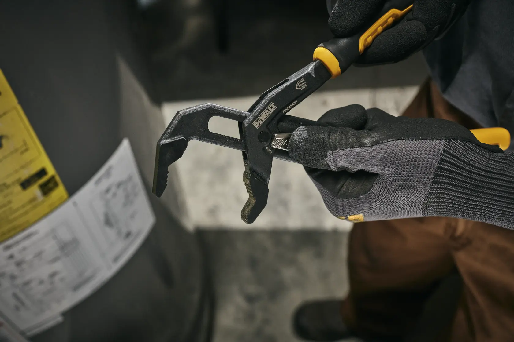 A person wearing gloves is holding a DEWALT adjustable groove joint plier tool, SKU DWHT82820, in a workshop setting.