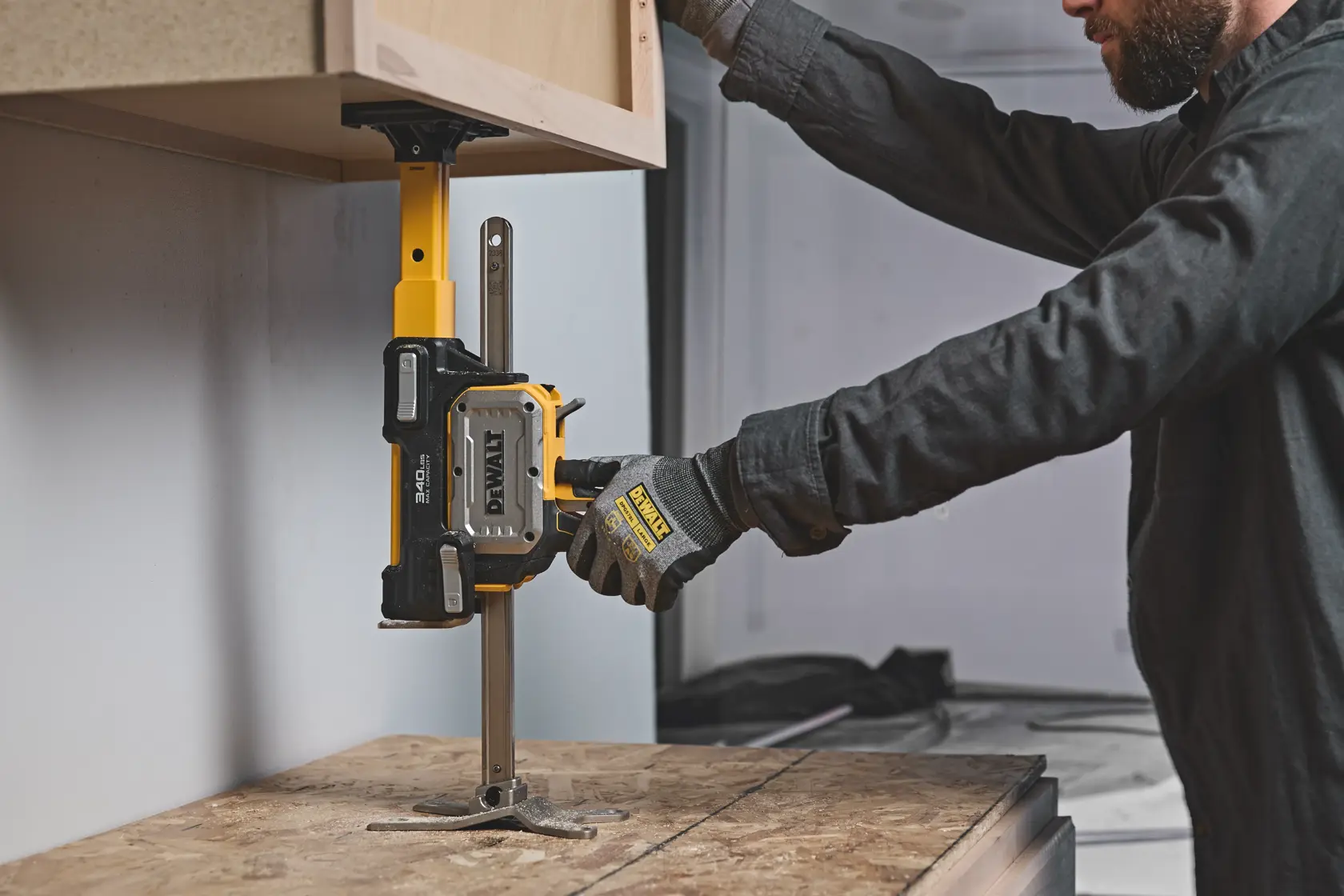 Person uses DEWALT cabinet jack to install upper cabinet onto wall. Tool supports cabinet for precise placement.