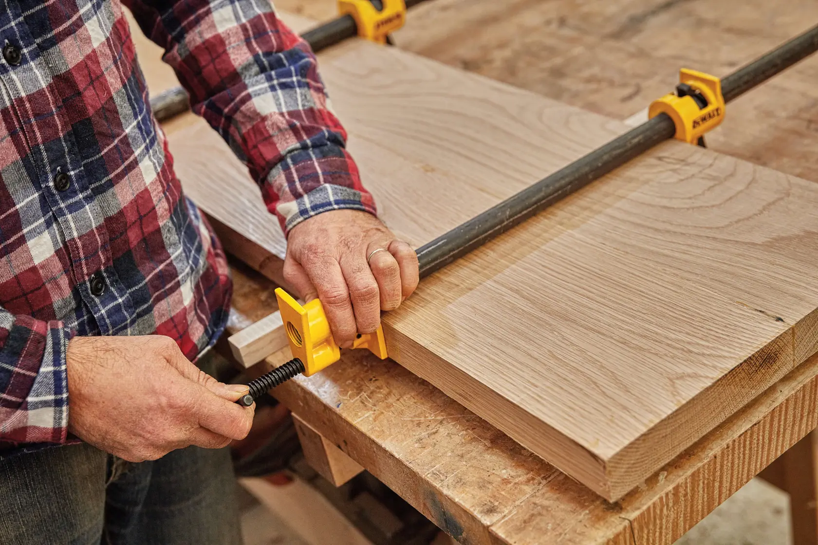 A person using a DEWALT pipe clamp to secure two pieces of wood together on a workbench.
