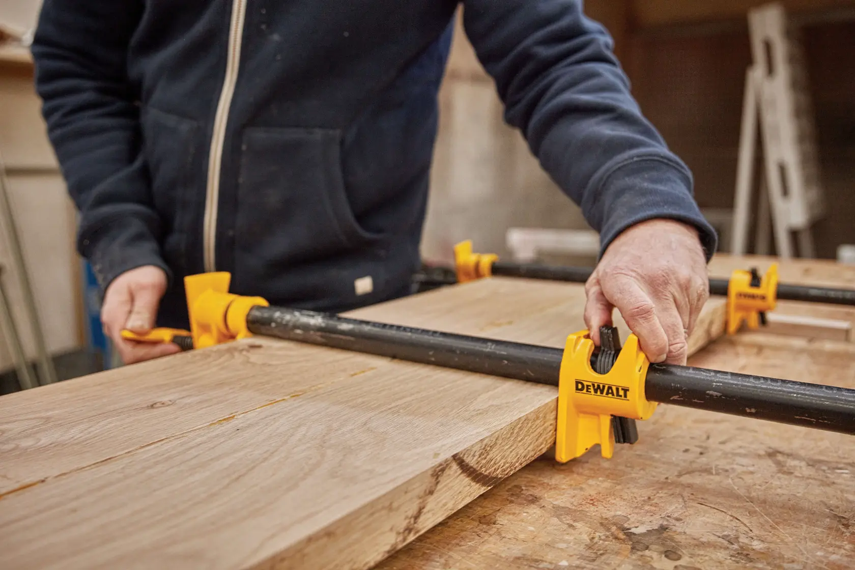 A person using DEWALT yellow pipe clamps to hold wooden boards together on a workbench.