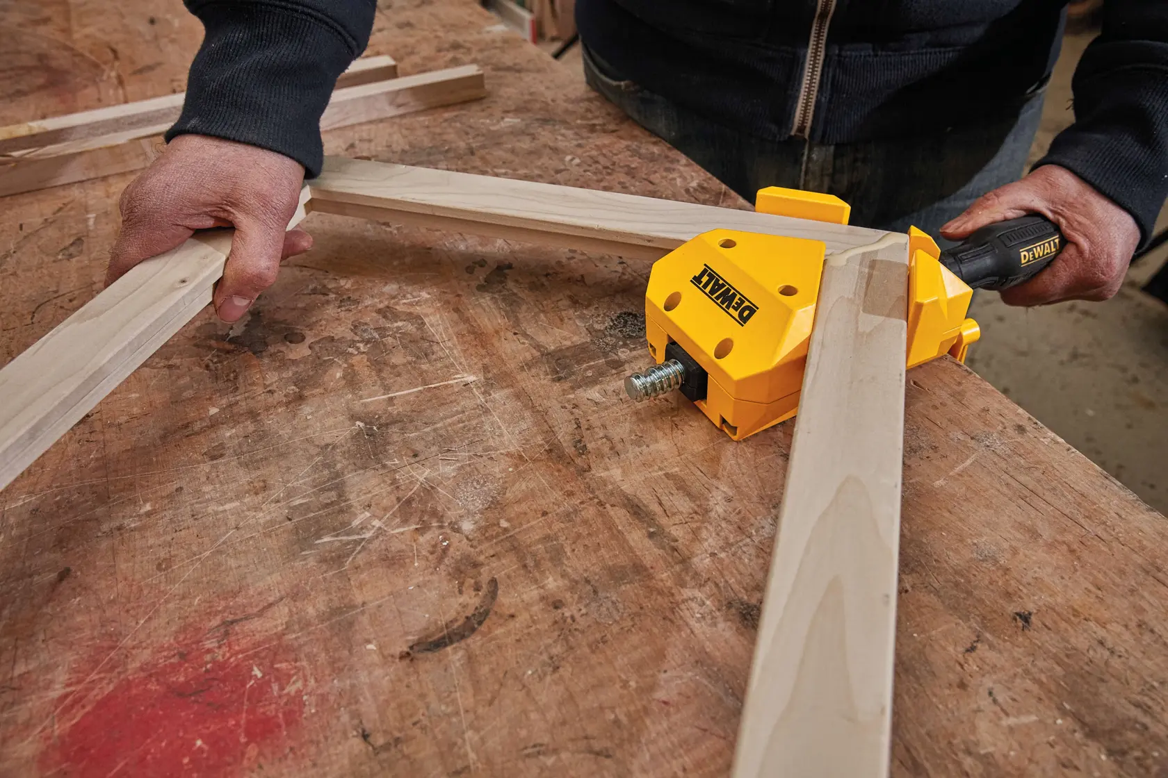 A person using a DEWALT corner clamp to hold two wooden pieces at a right angle on a workbench, ideal for woodworking and frame assembly.
