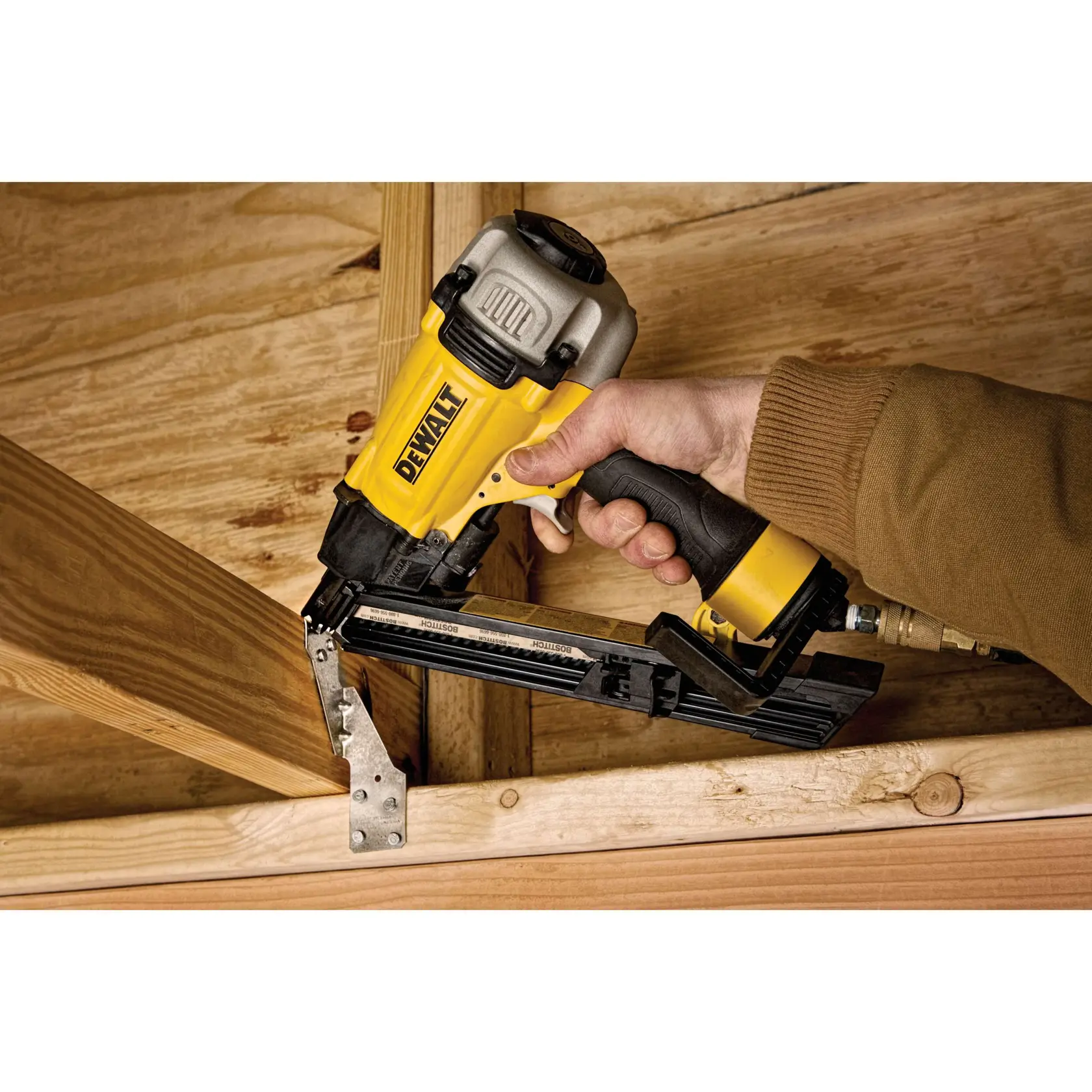 A person is using a DEWALT pneumatic nail gun to fasten a metal connector to wooden beams during construction.