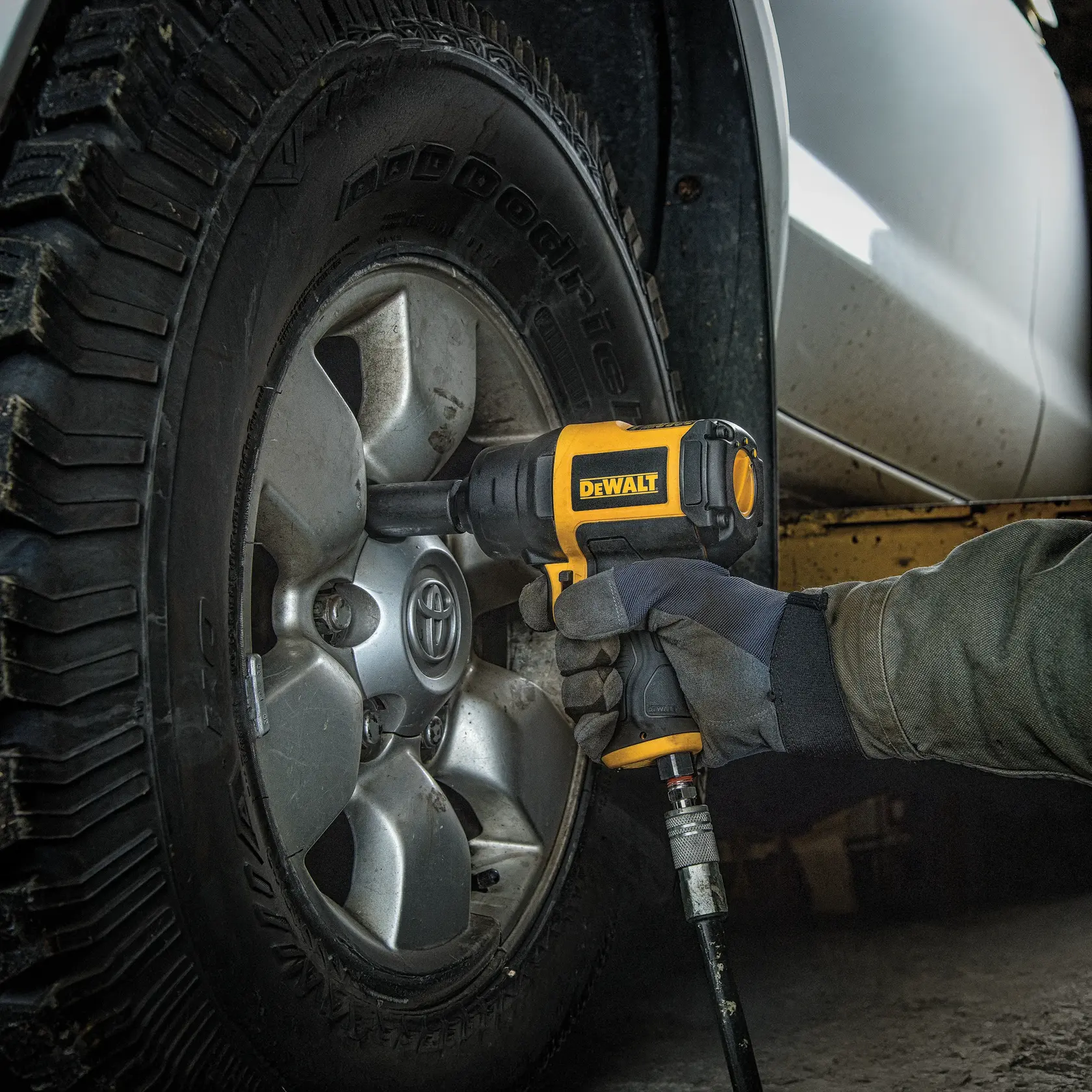 A person using a DEWALT pneumatic impact wrench to tighten or loosen the lug nuts on a car wheel.