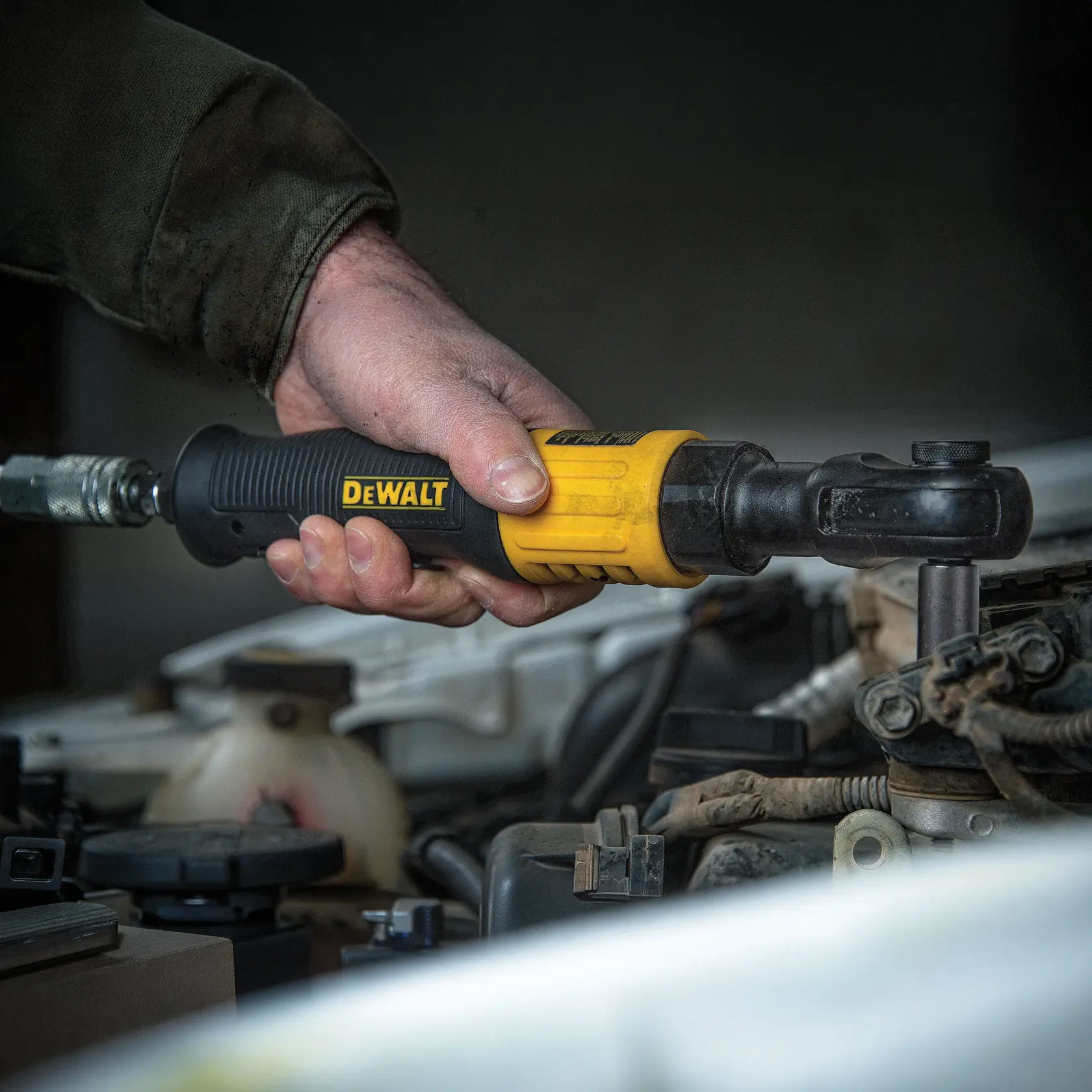 A hand using a DEWALT pneumatic ratchet tool to tighten a bolt on a car engine.